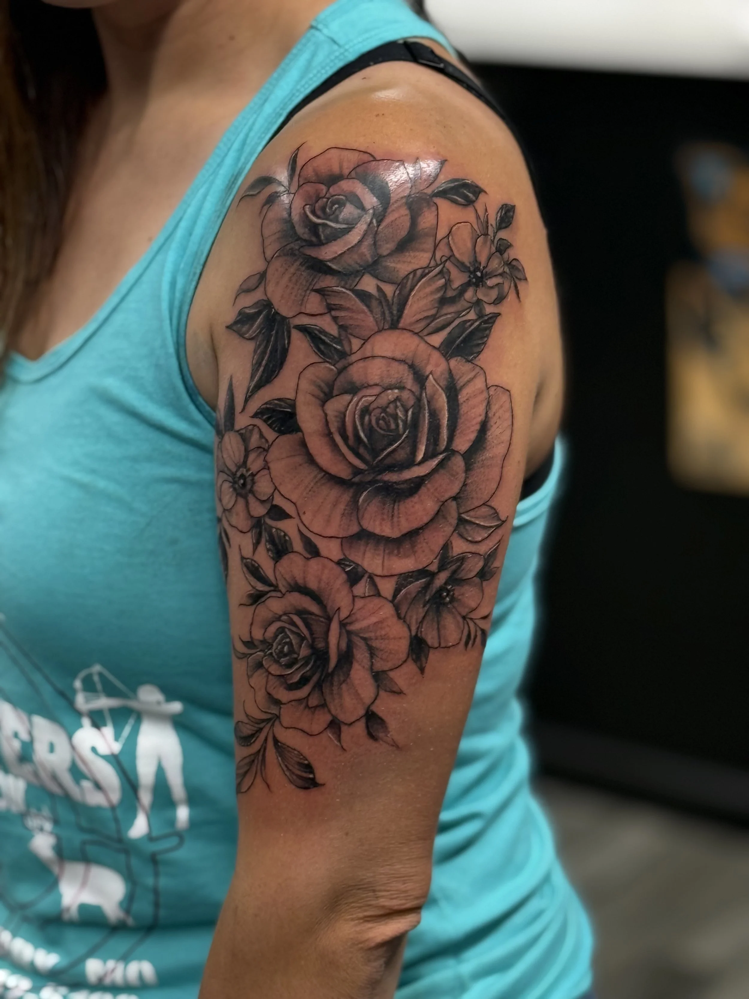 A person's upper arm with a detailed black and gray floral tattoo featuring roses and other flowers.