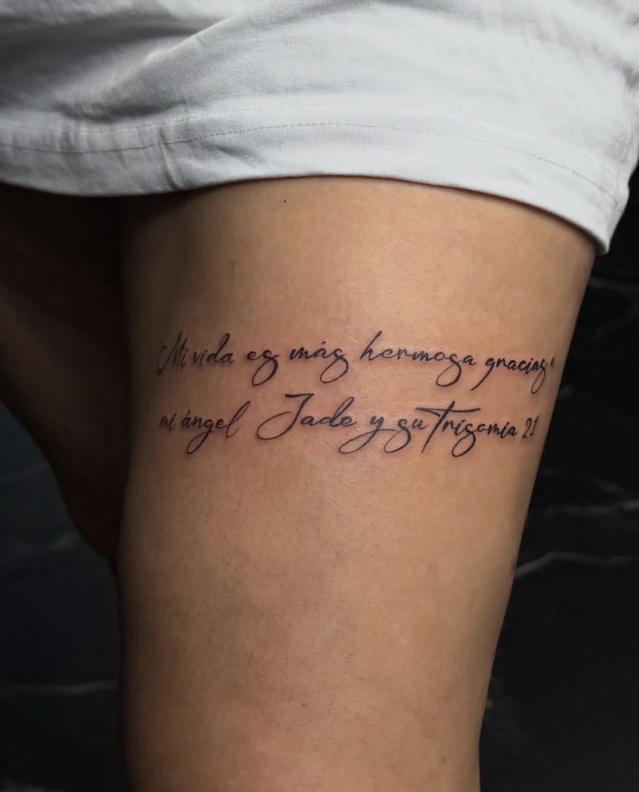 Tattoo on a person's thigh with Spanish text that reads: "Mi vida es más hermosa gracias a mi angel Jade y gu trisimo?!"