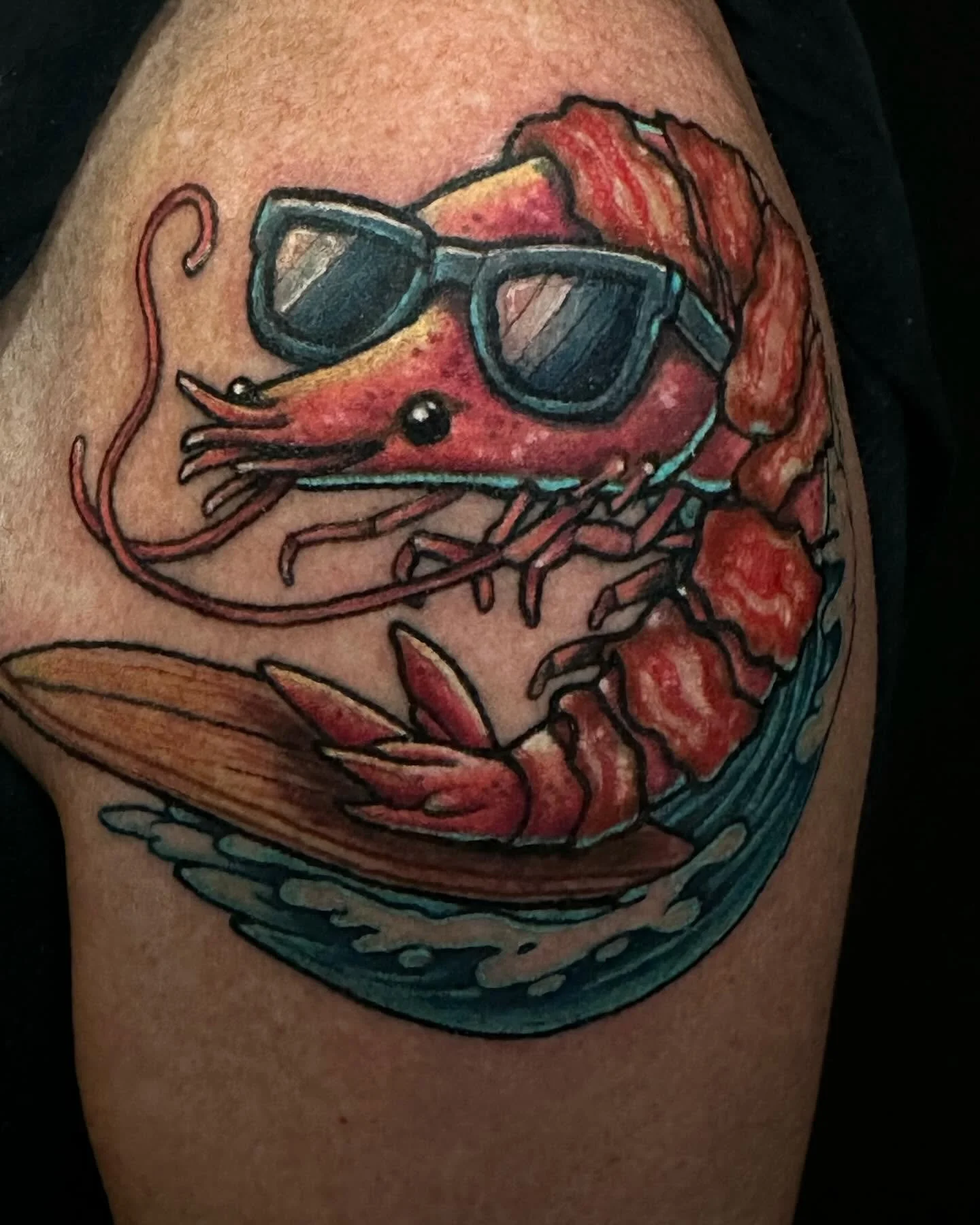 A tattoo of a shrimp wearing sunglasses with a red background and some orange accents.