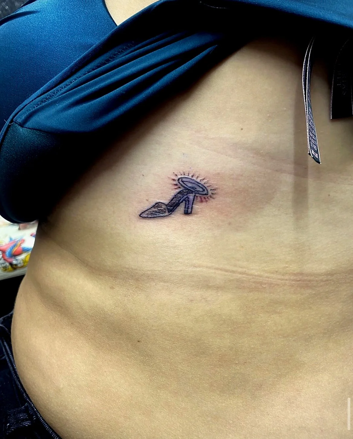 A tattoo of a high-heeled shoe with a halo and a shining effect on the person's side.