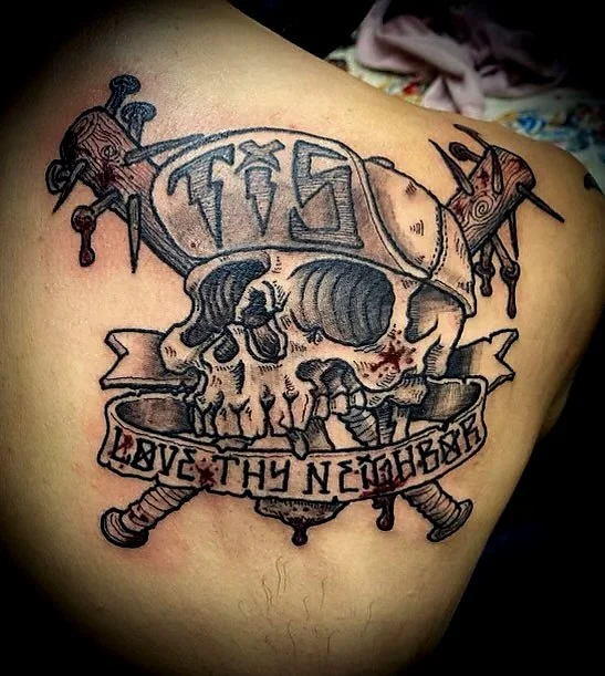 A tattoo of a skull wearing a knight's helmet with a sword through it, surrounded by two crossed swords and a banner that reads "LOVE THY NEIGHBOR."