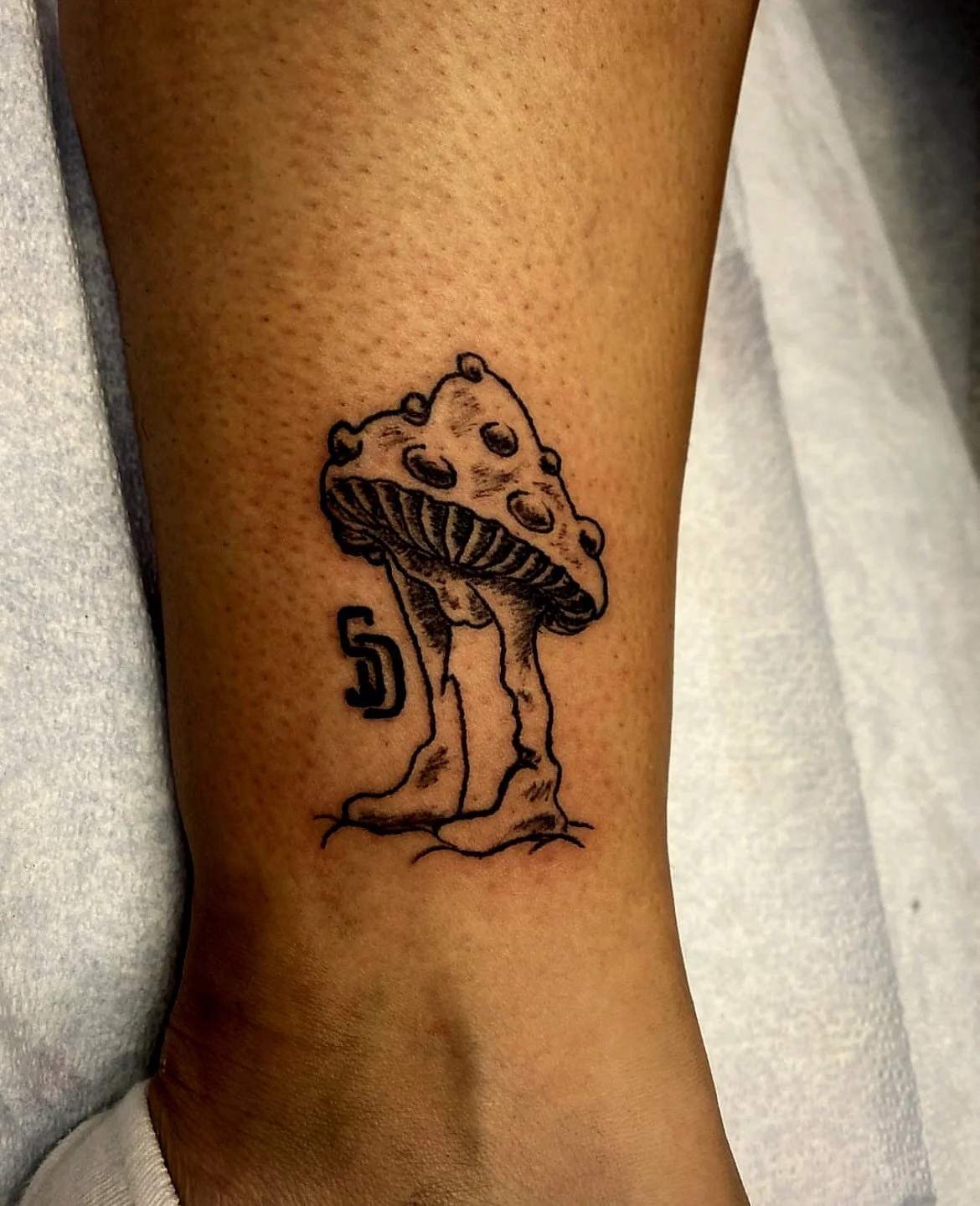 A tattoo of a cartoonish mushroom with a cartoonish face, placed on a person's arm.