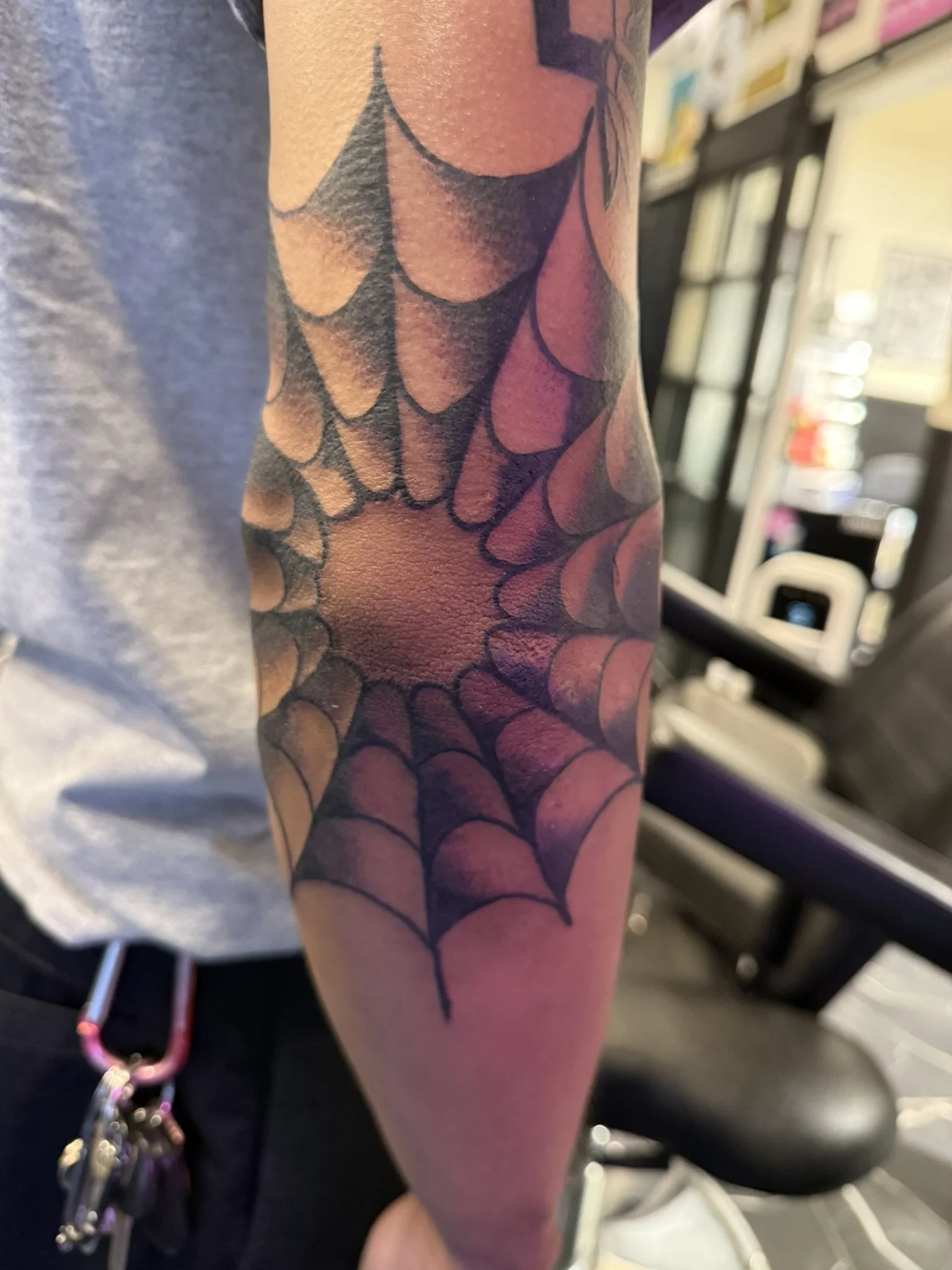 Close-up of a person's arm with a tattoo of a spider web pattern in black ink.