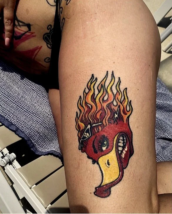 Tattoo of a flaming anatomical heart on a person's thigh, featuring a red and yellow color scheme and bandages.