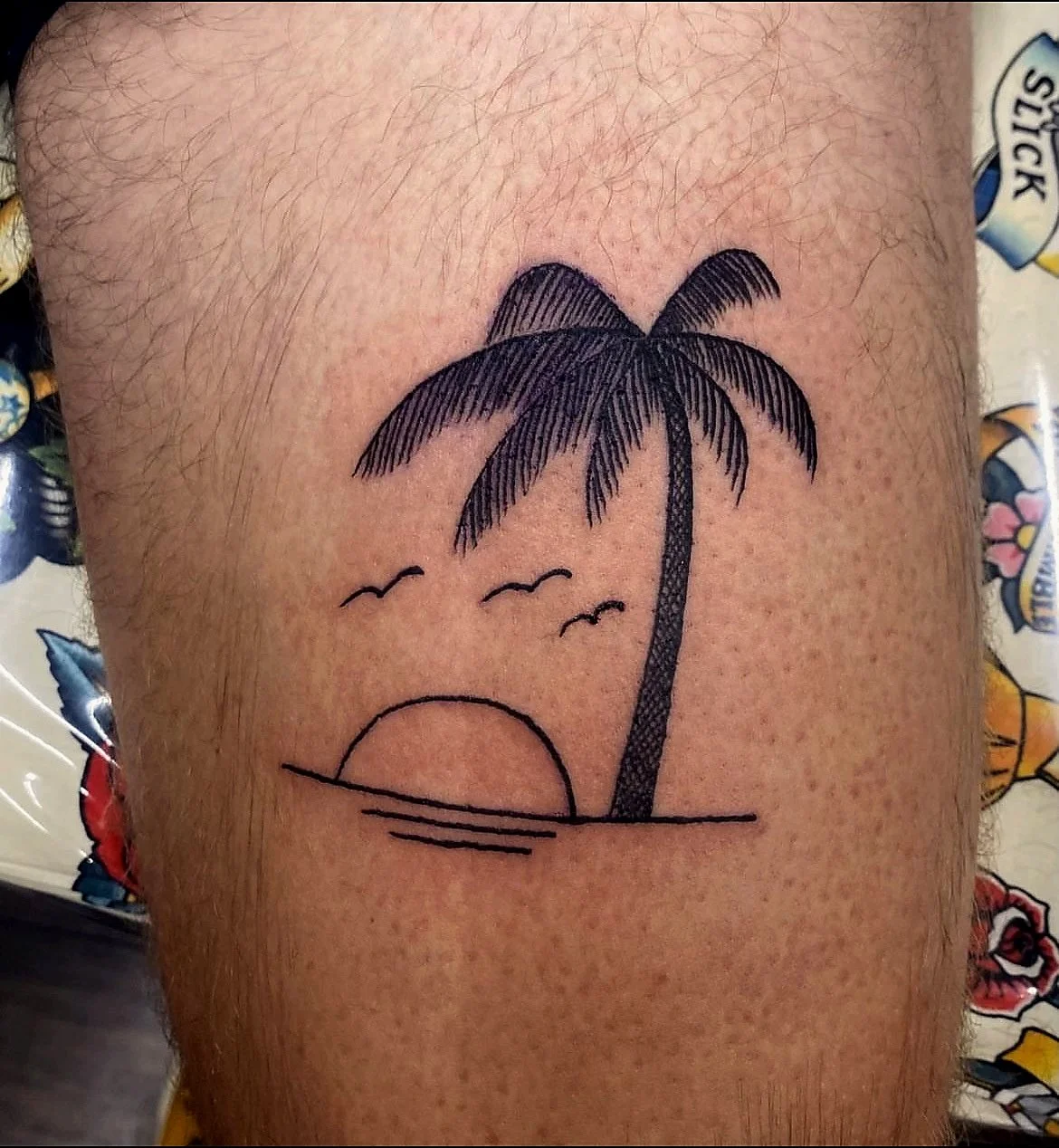 Tattoo of a minimalistic sunset with a palm tree, seagulls, and sunset lines on the skin.