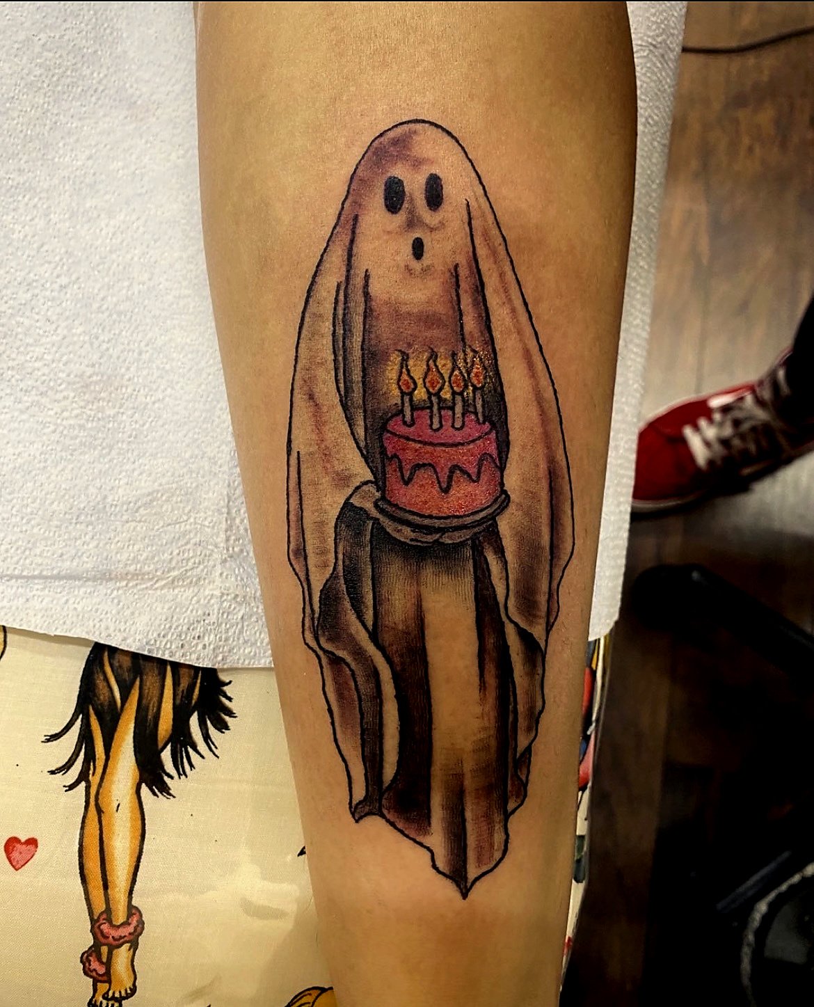 Tattoo of a ghost holding a birthday cake with candles.