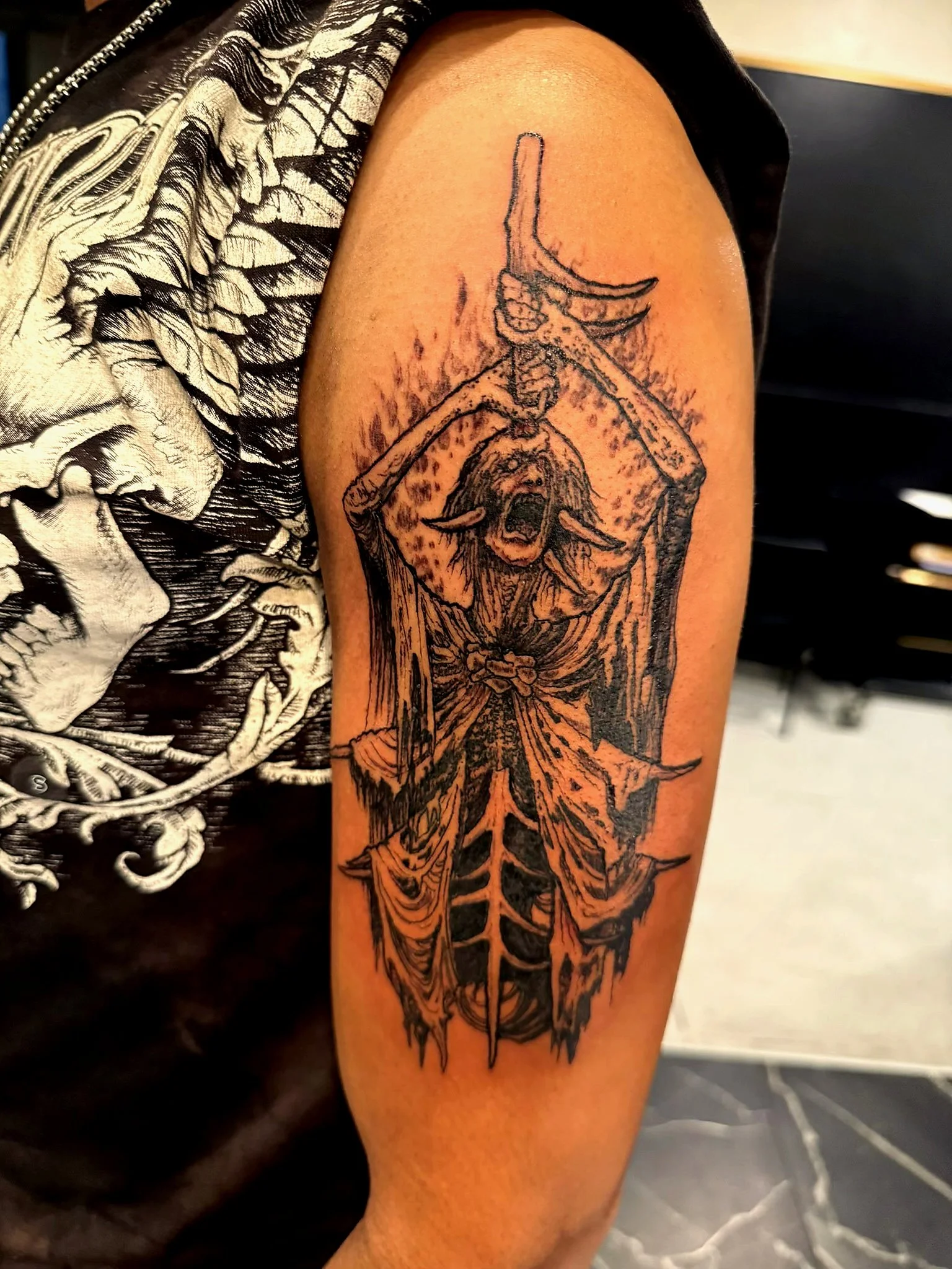 Tattoo of a crying goat skull with horns, holding a sword, on a person's upper arm