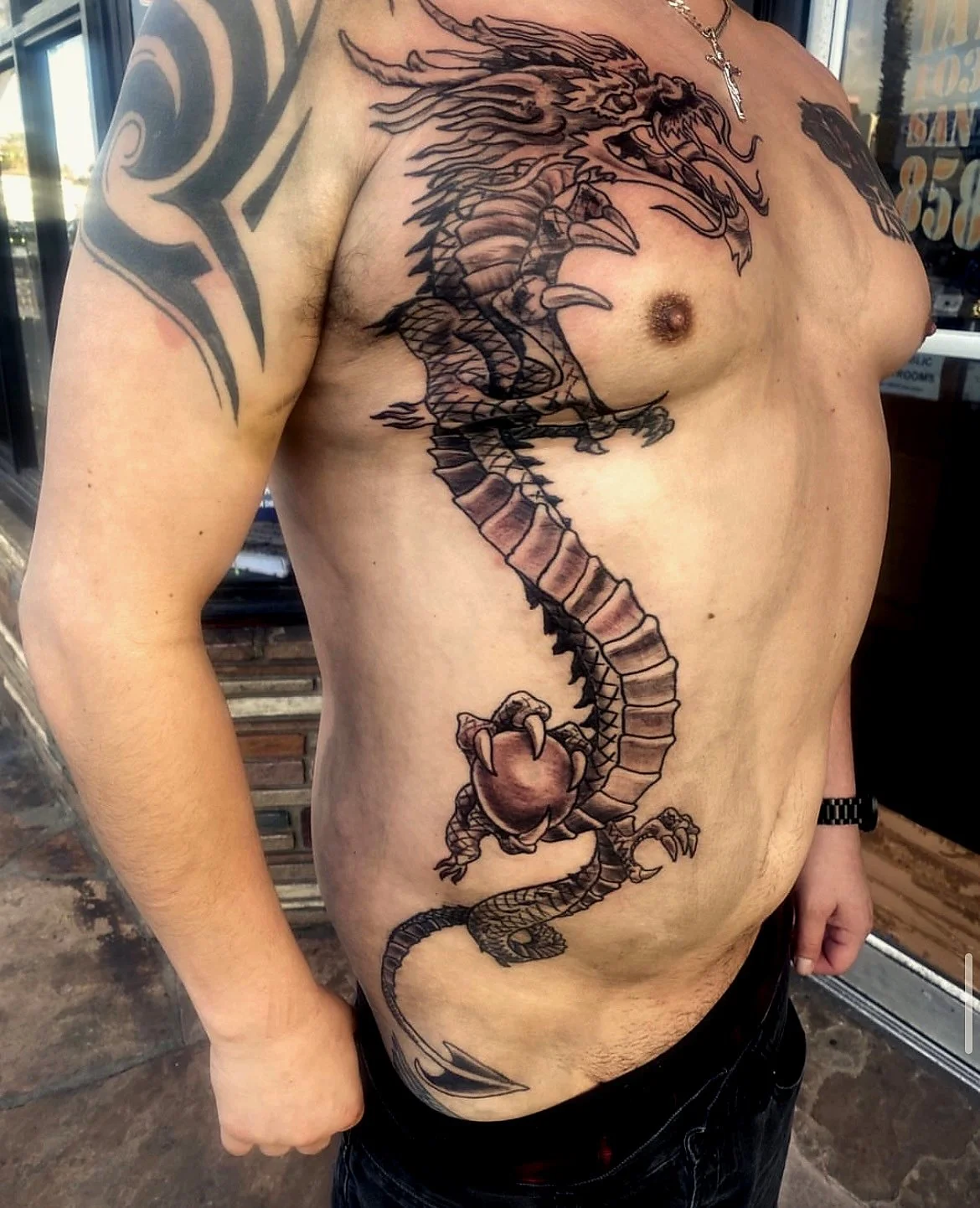 A large black and gray tattoo of a dragon covering the person's chest, side, and waist.
