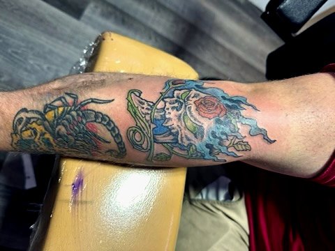 A person's forearm with a colorful tattoo of a lion's head surrounded by blue flames.