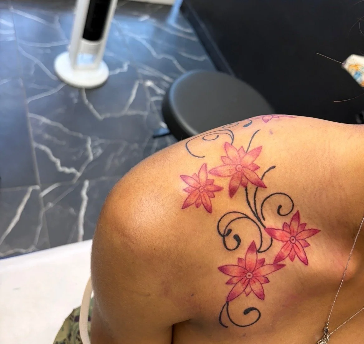 Tattoo of pink flowers with black swirling stems on a person's shoulder in a tattoo shop.