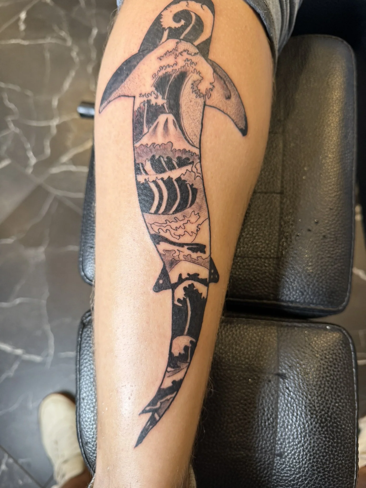 Tattoo of a large whale, possibly a sperm whale, with ocean waves and a mountain in the background, on a person's upper arm.