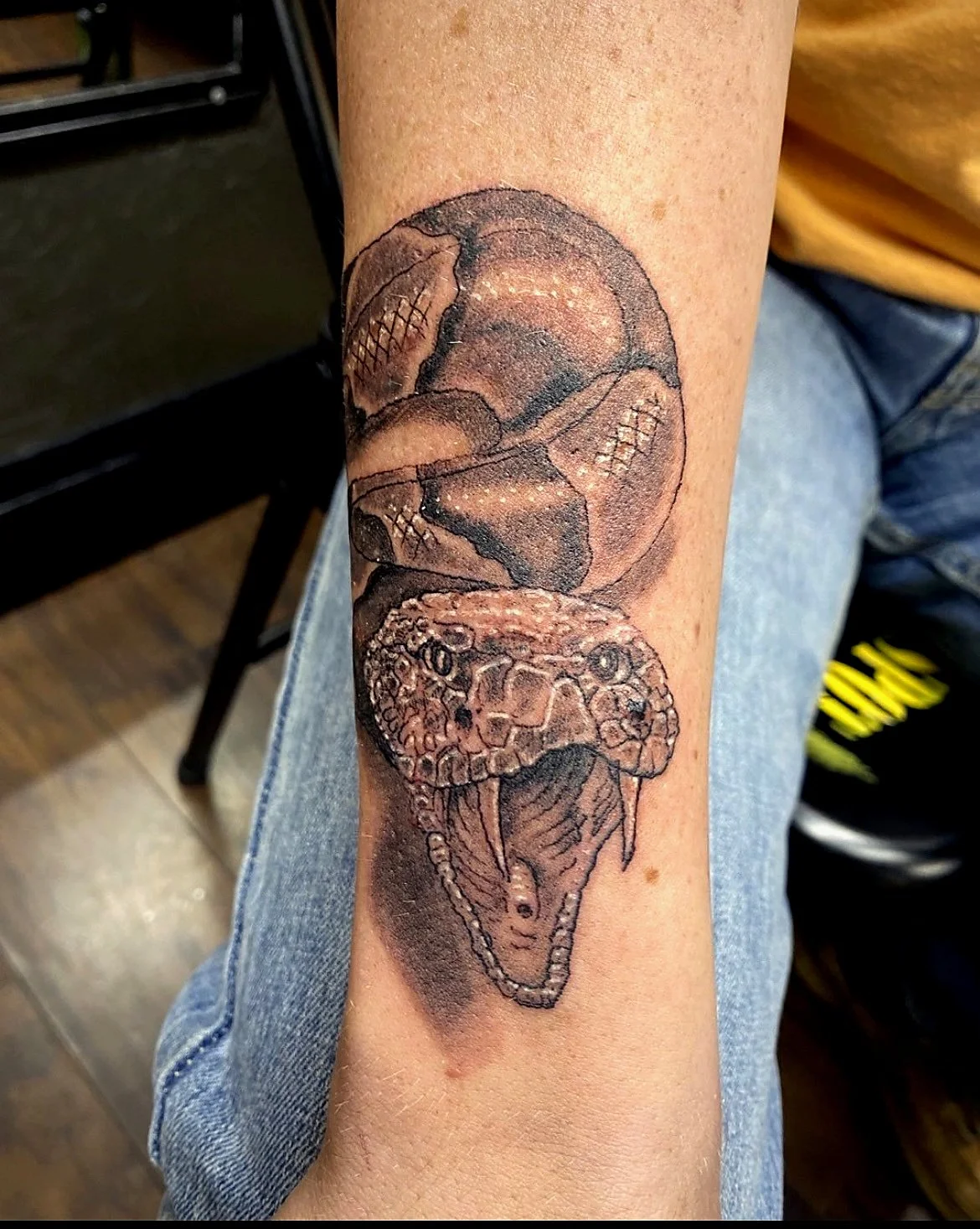 A tattoo of a snake's head with its mouth open, revealing fangs, on a person's forearm.