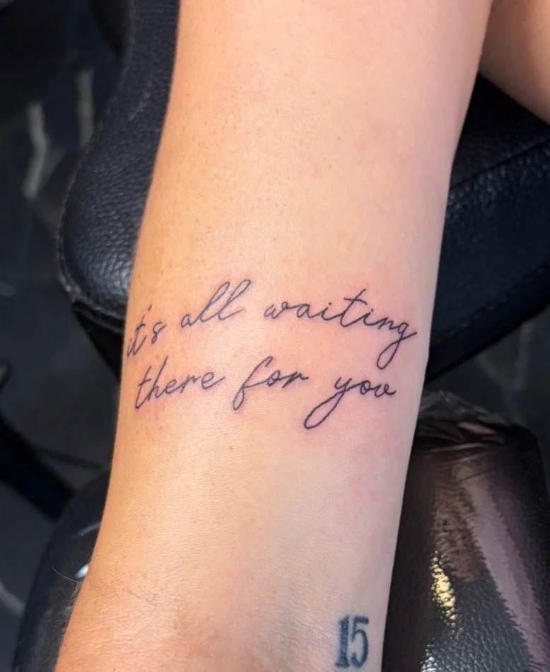Tattoo on person's forearm reading 'it's all waiting there for you' in cursive script.