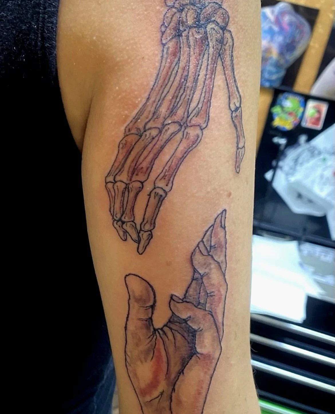 Tattoo of a skeletal hand and a realistic hand on a person's arm.