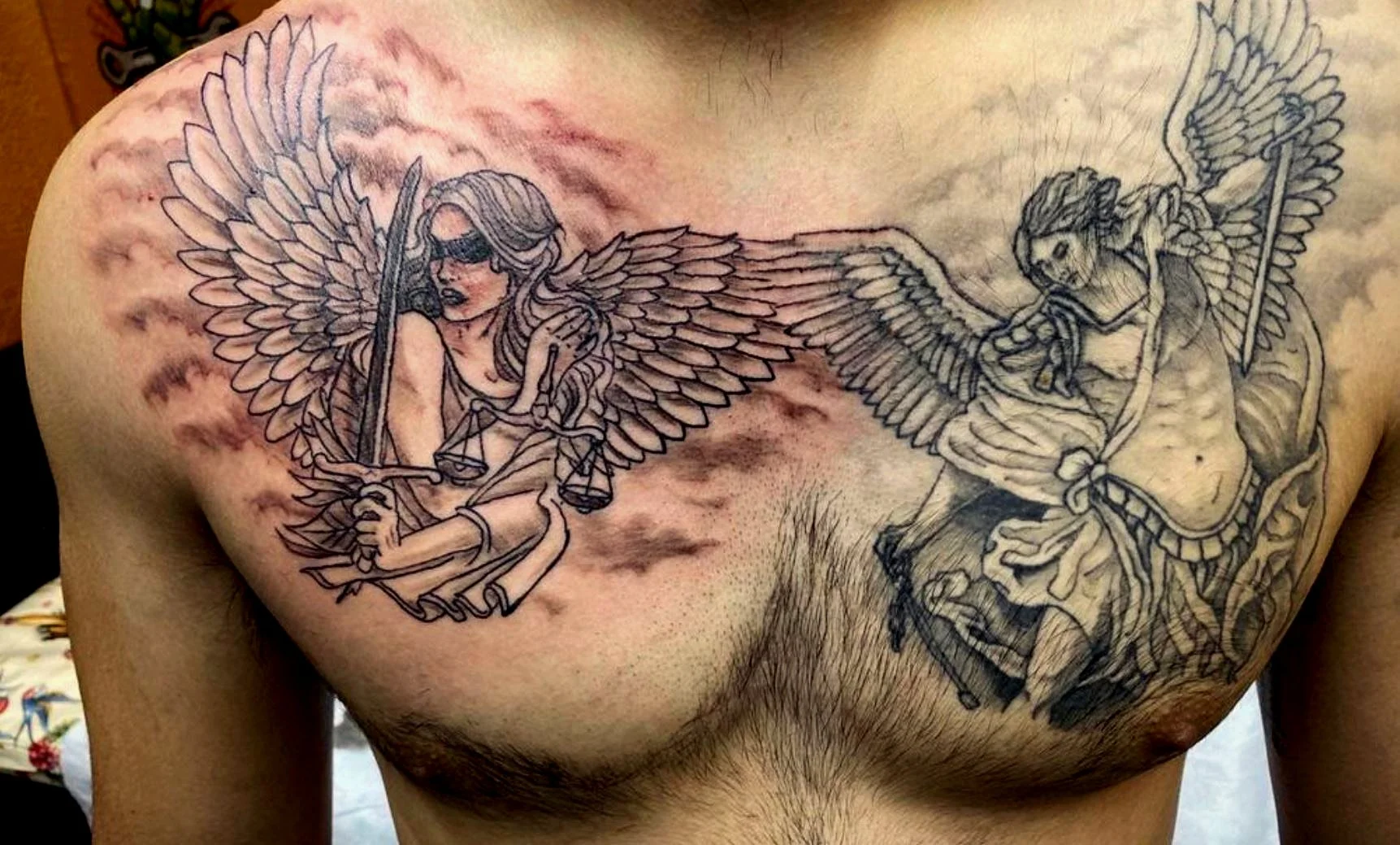 A tattoo of two winged figures on a person's chest, a woman with scales and blindfold holding a sword, and an angel with a spear and shield.
