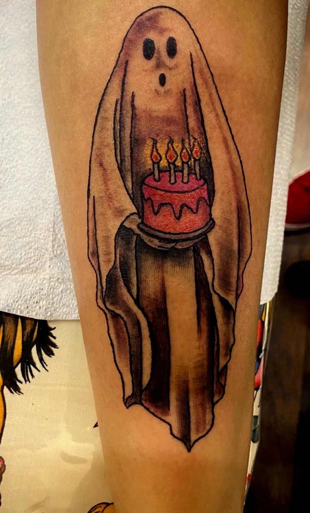 A tattoo of a ghost holding a birthday cake with lit candles.