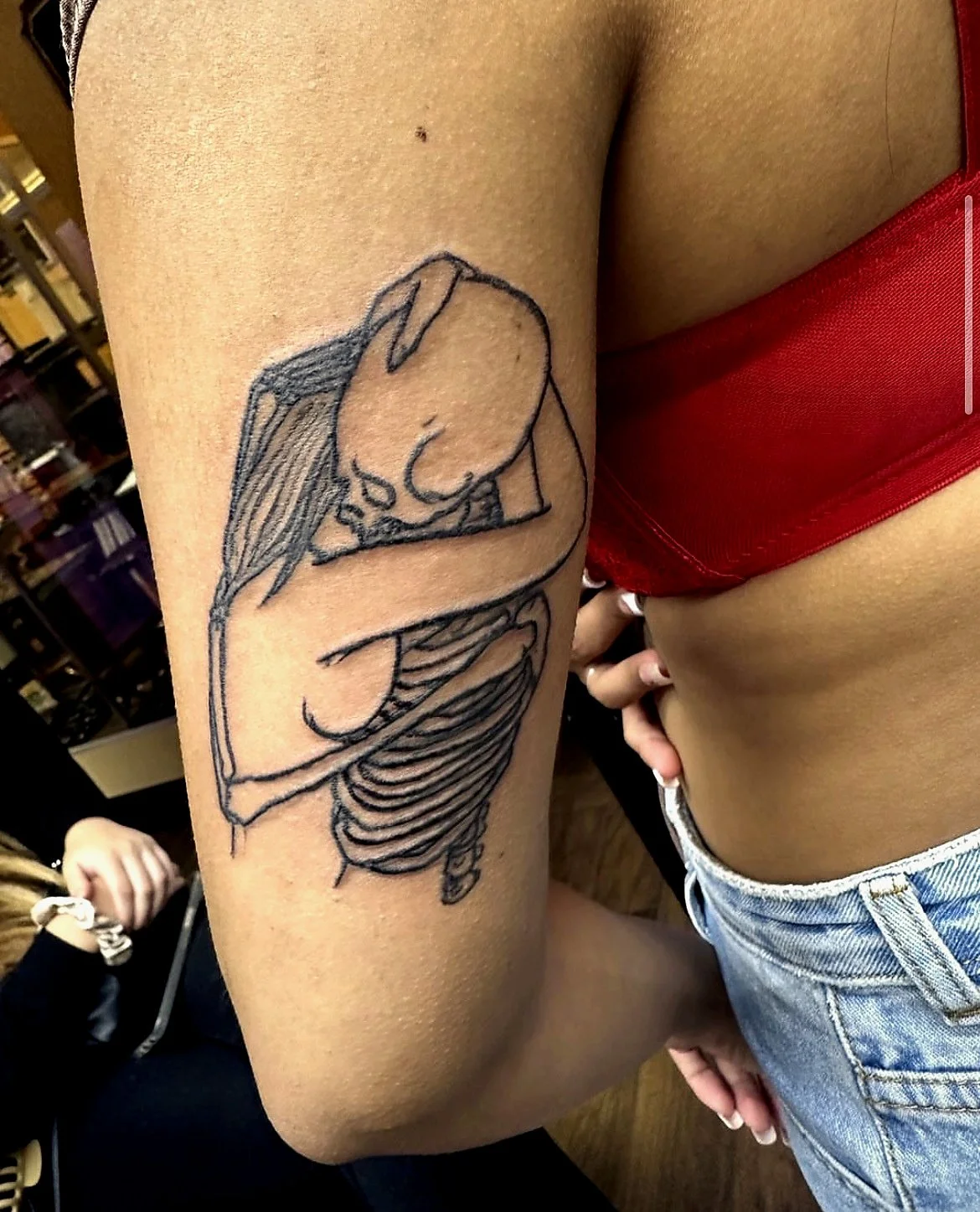 Tattoo of a minimalist line drawing of a woman with long hair resting her head on her arm on a person's upper arm.