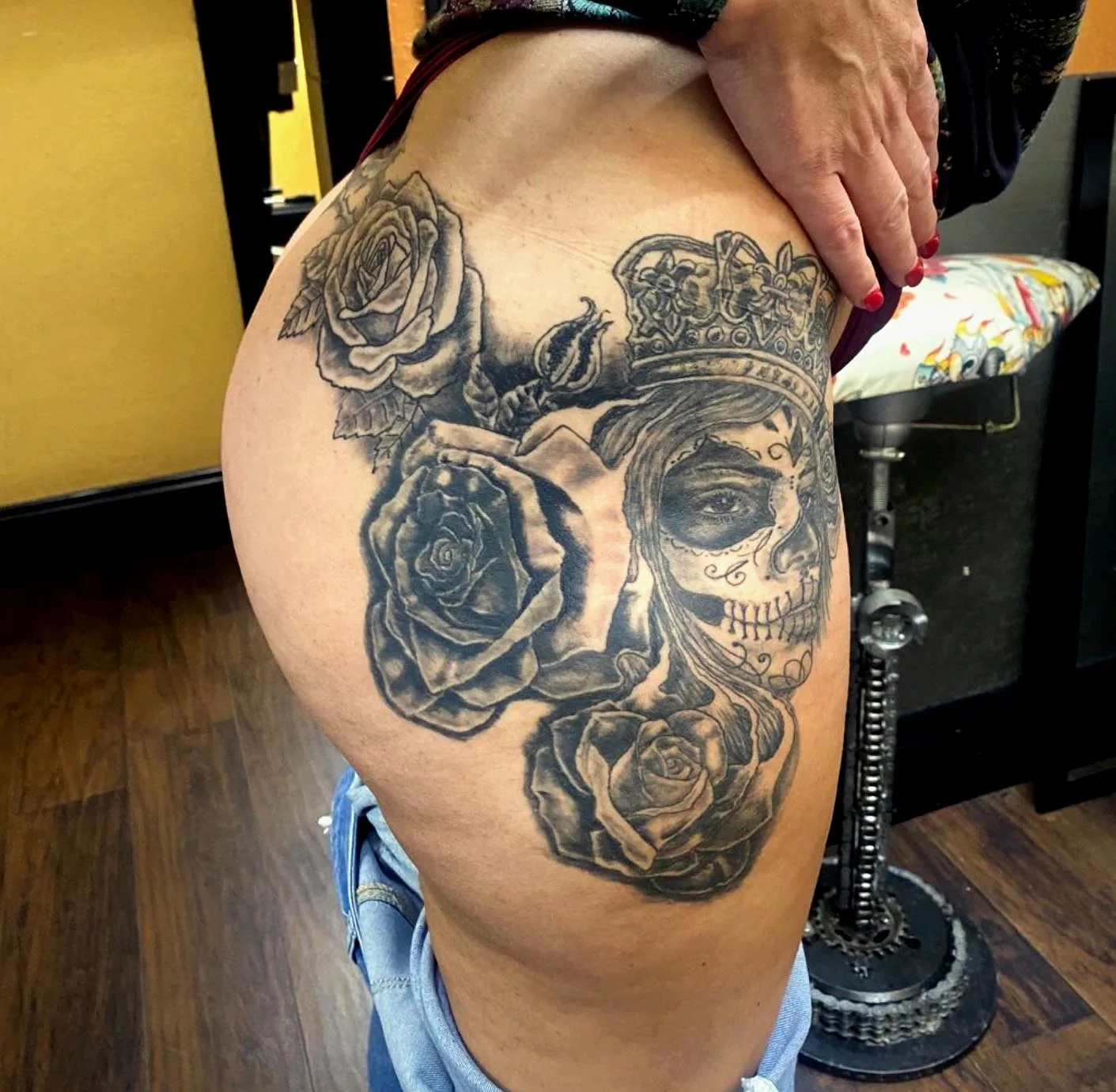 A tattoo of a woman's face with makeup and a crown, surrounded by roses, on a person's upper thigh.