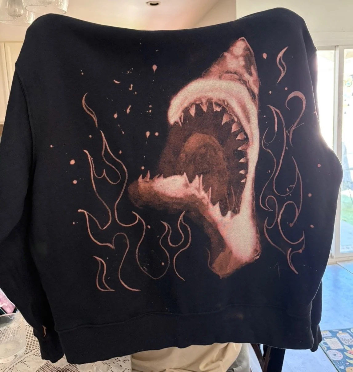 Black sweatshirt with a graphic of a roaring shark with sharp teeth, surrounded by swirling lines and abstract splatters.