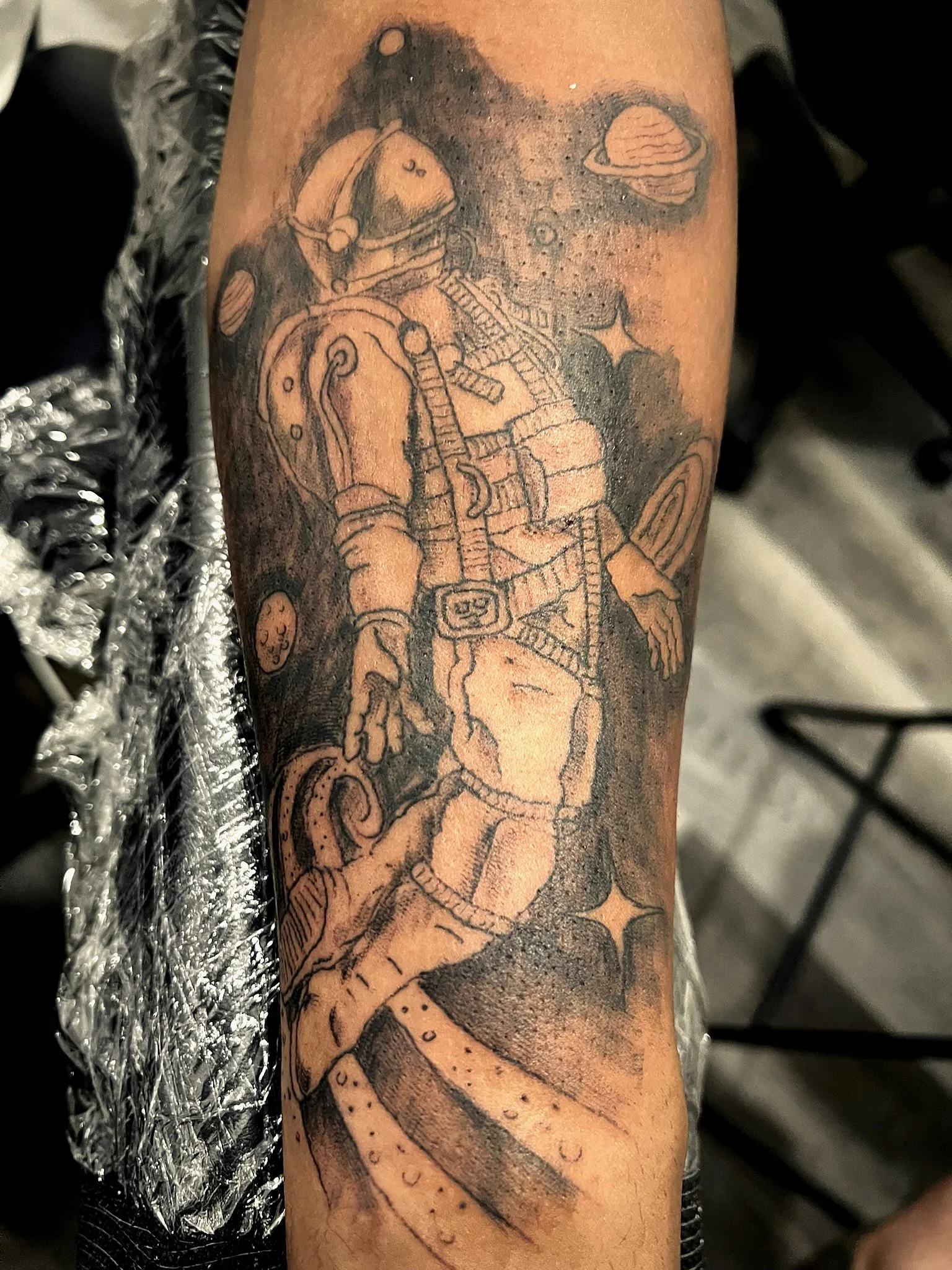 A tattoo of a robot astronaut holding a rocket and standing on an alien planet with a single star, several planets, and stars in the background.