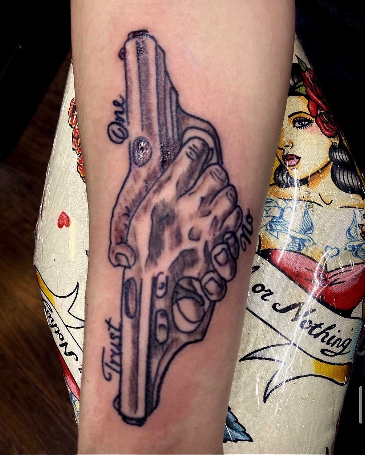 Tattoo of a hand holding a gun with the words "Thank You" and "One" written around it.