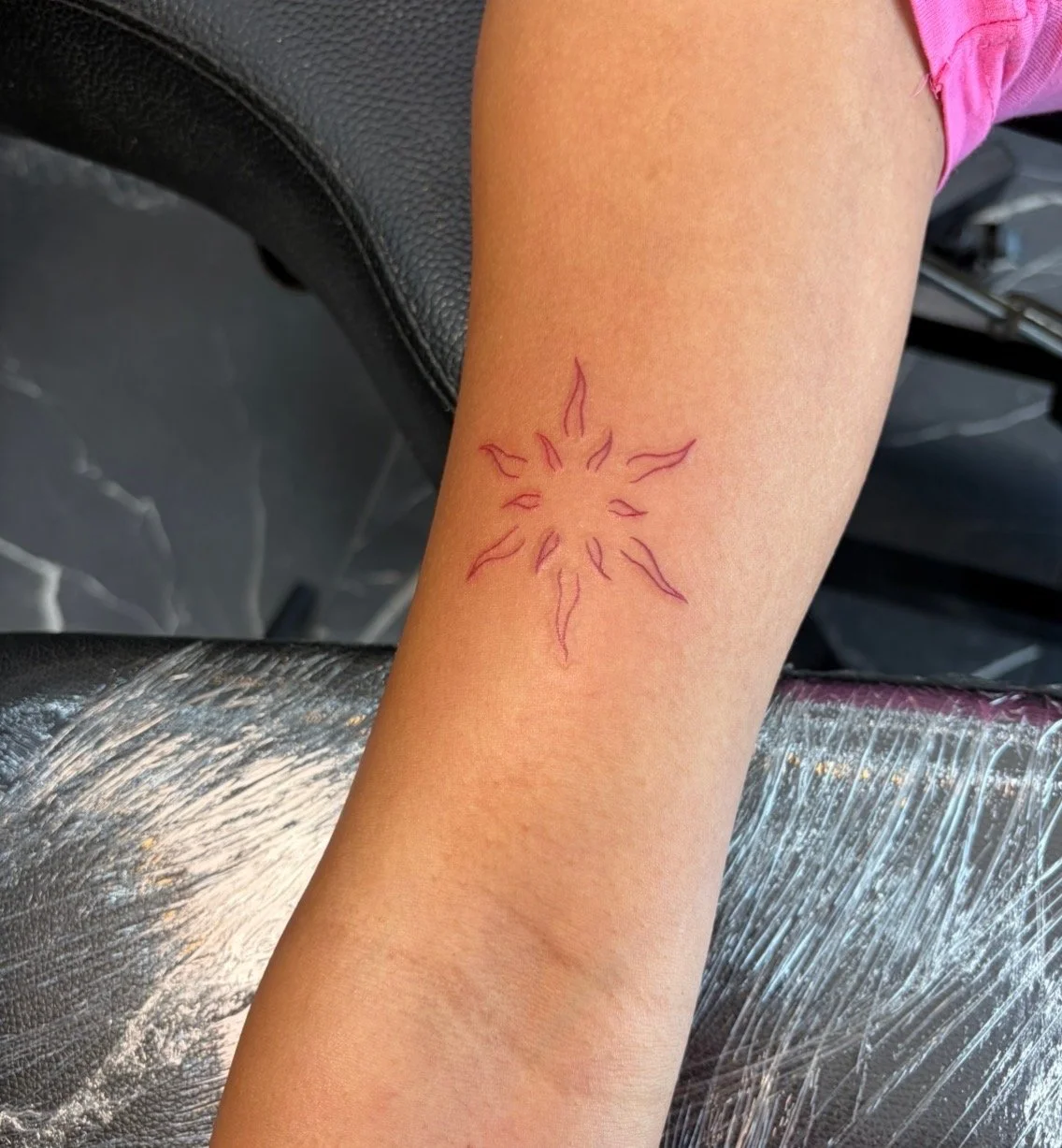 A freshly done tattoo of a sun with flames is on a person's forearm.
