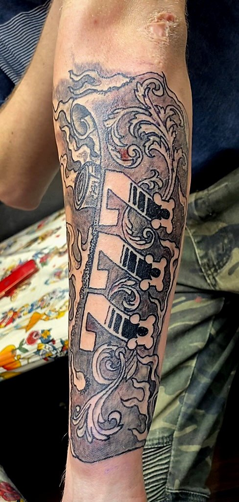 Tattoo of a key with decorative swirls on a person's forearm.