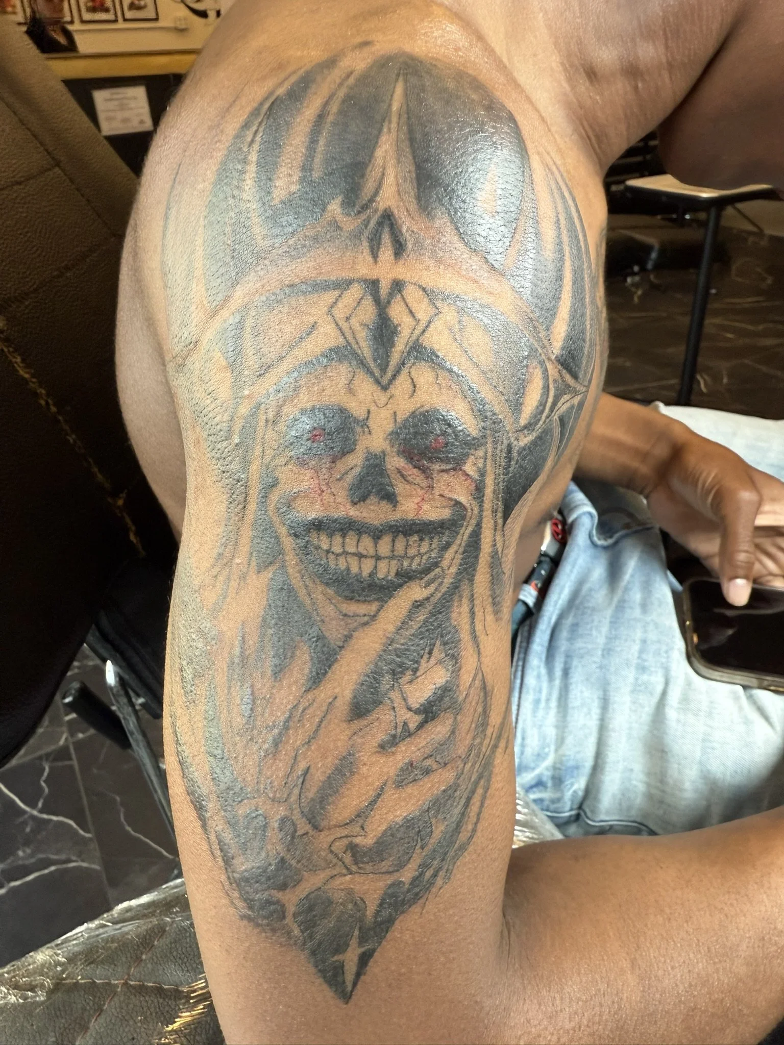 A tattoo of a skull with a bat-like face and outstretched wings on a person's upper arm.