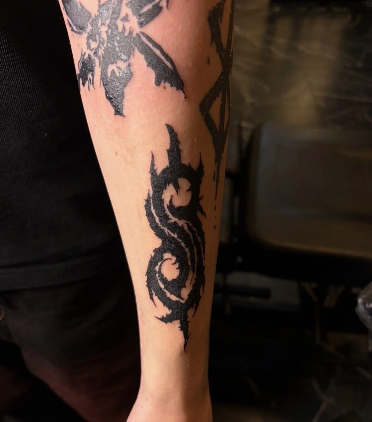 Black tribal tattoo on person's arm with swirling and jagged patterns.