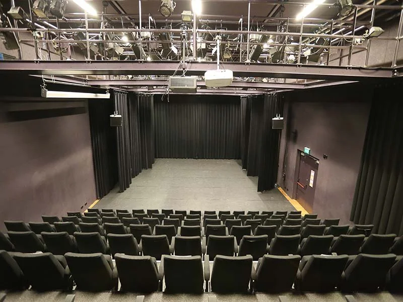 Empty auditorium with black curtains, chairs, and a small stage.