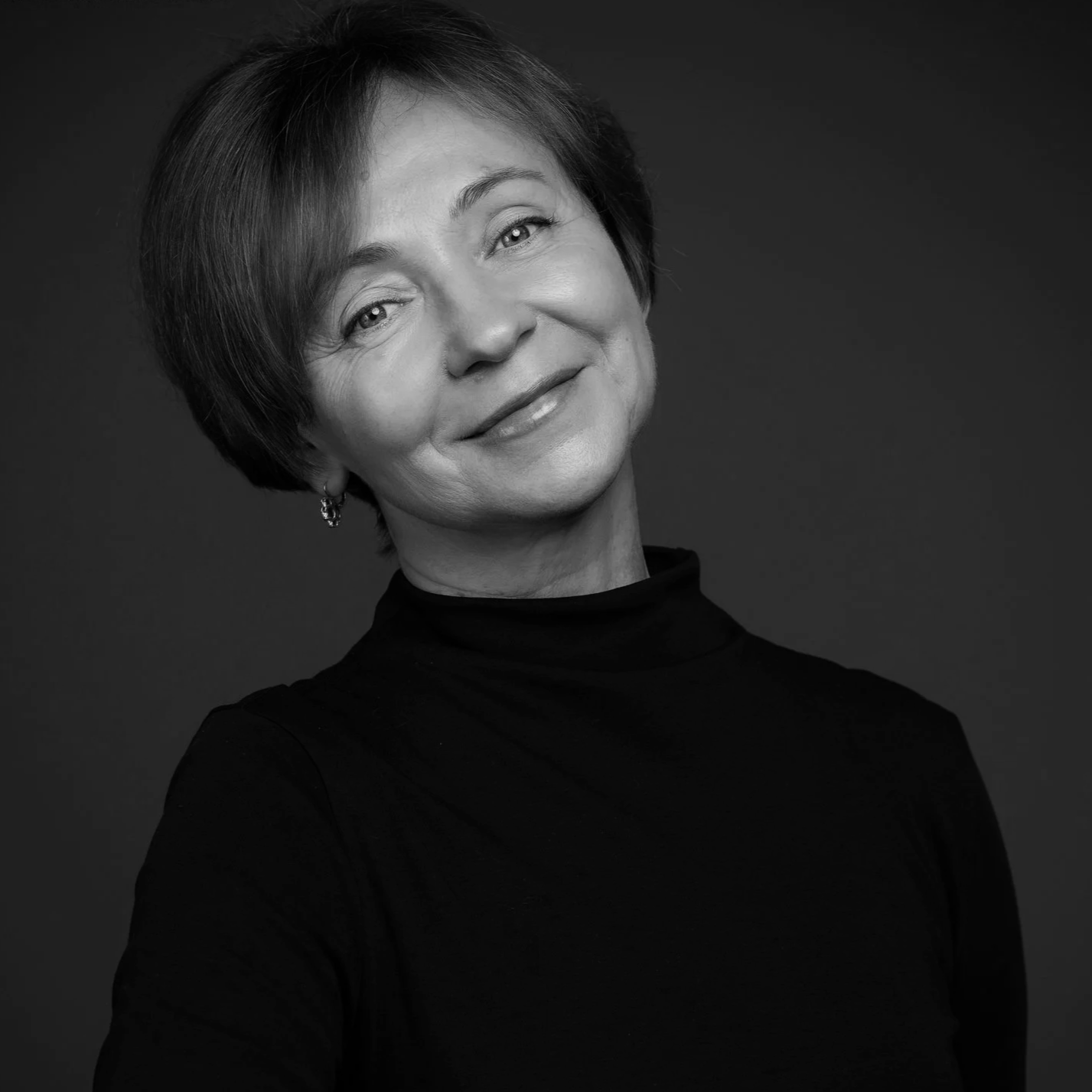 Black and white portrait of a smiling middle-aged woman with short hair, wearing a turtleneck and earrings.