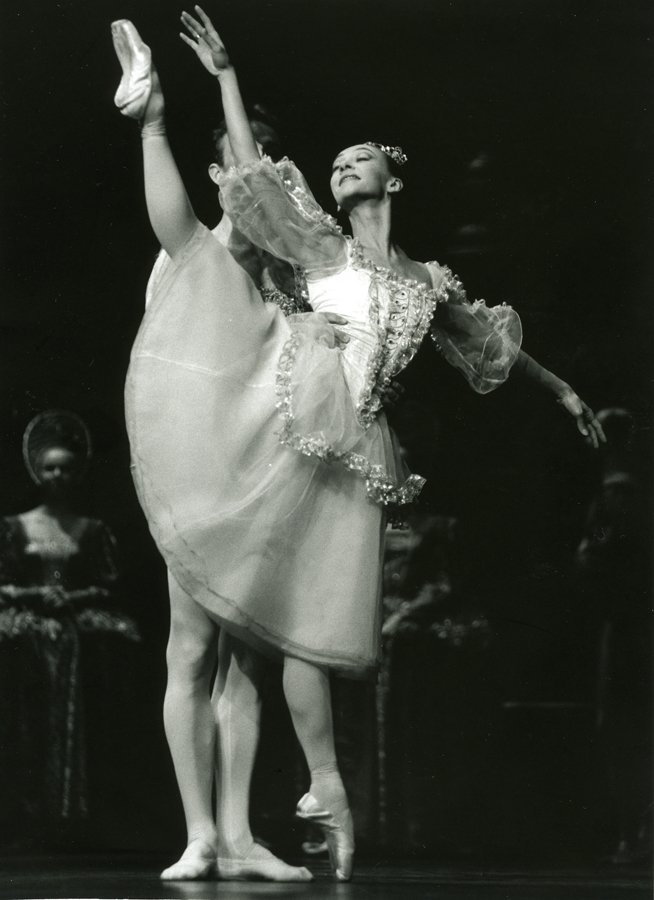 Two ballet dancers performing on stage, with one dancer lifting the other who is en pointe, wearing classical costumes.