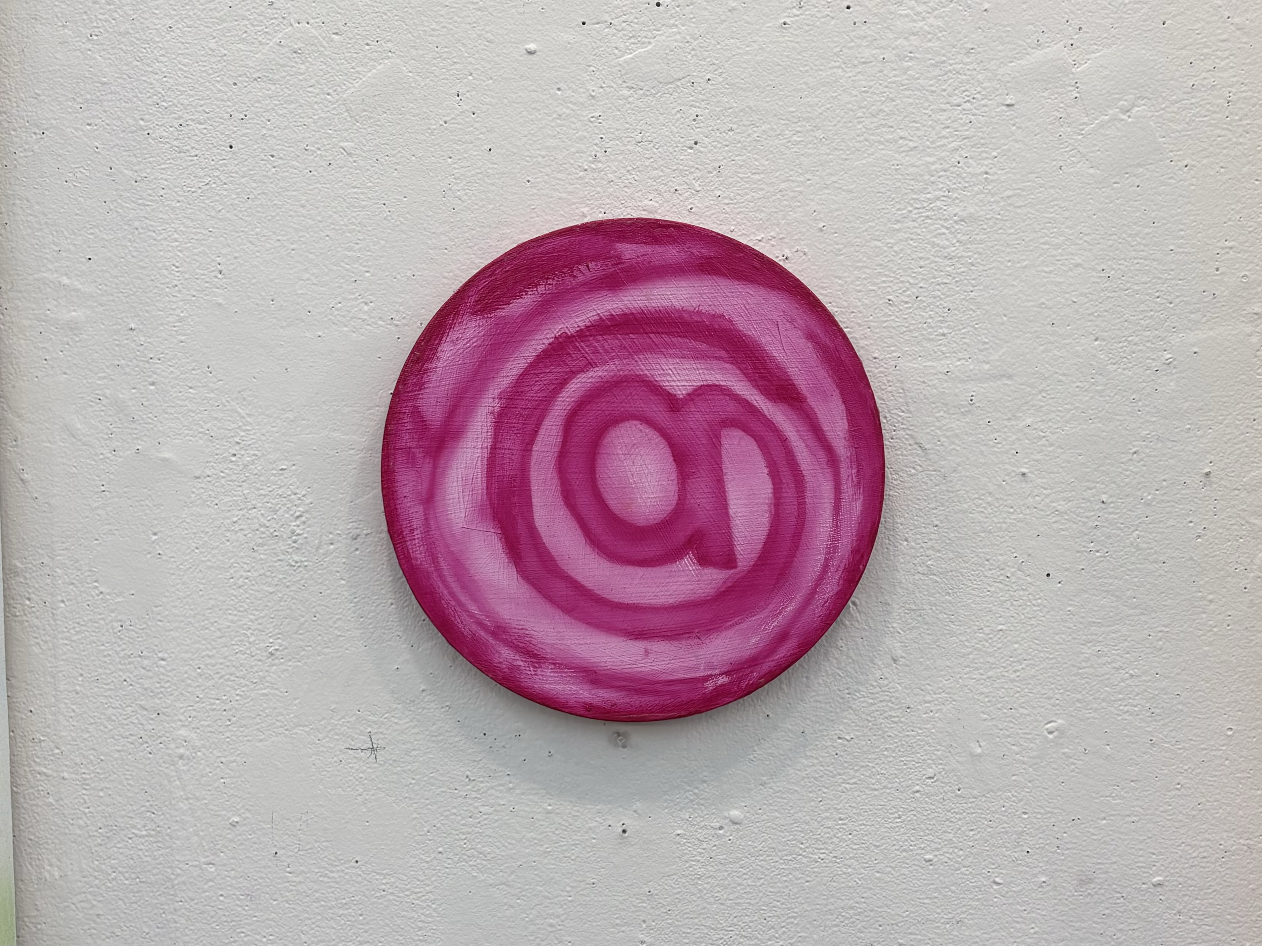 A pink and purple circular acrylic paint design on a textured white wall.