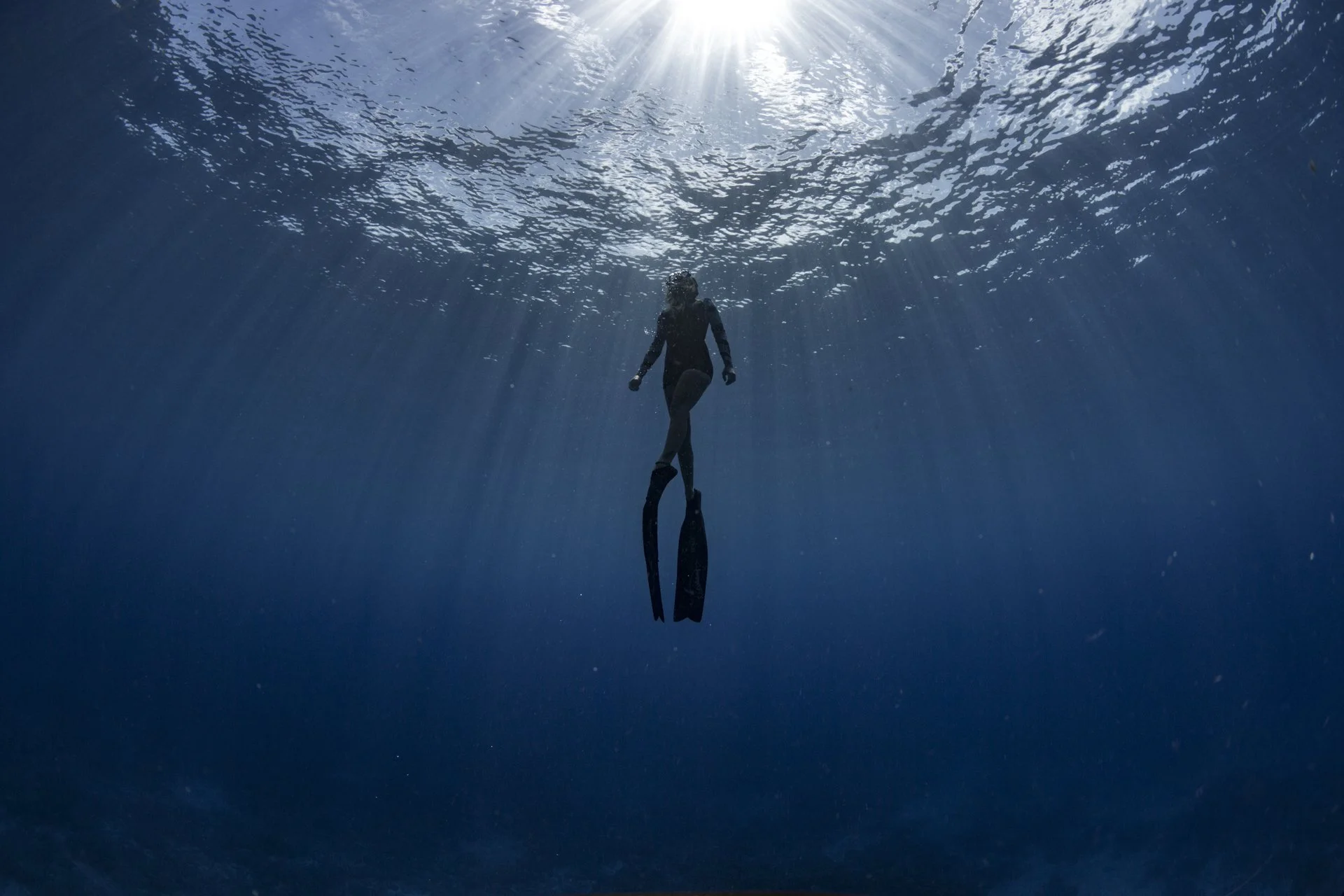 A person swimming underwater with sunlight shining through the water surface above.
