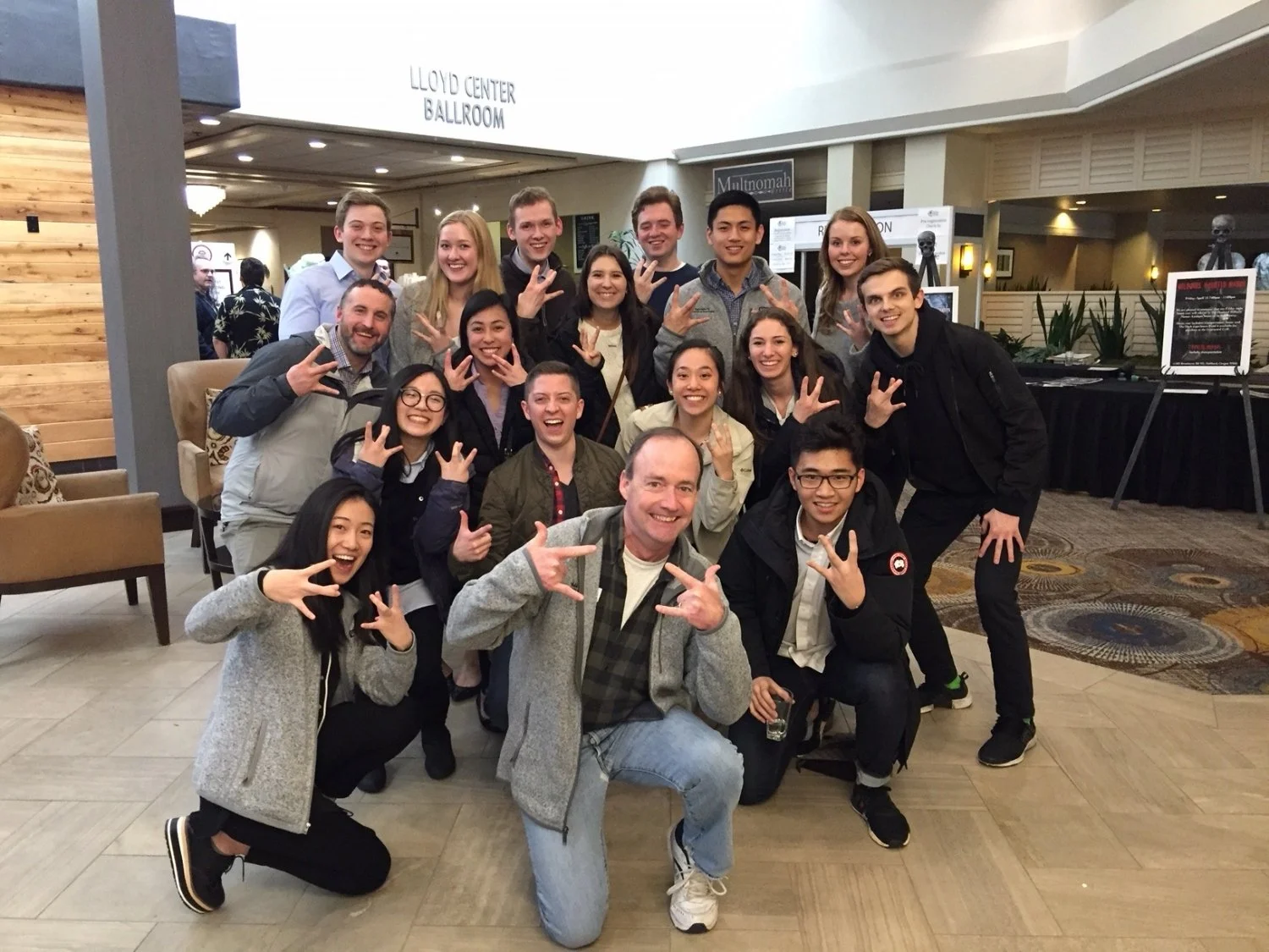 Group of people posing and smiling in a hotel lobby near the Lloyd Center Ballroom.