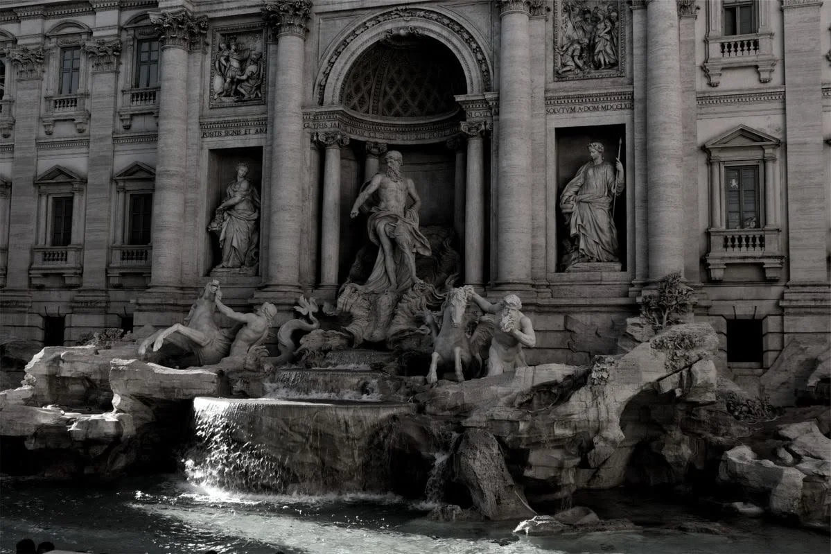 Fontana di Trevi a Roma con sculture di figure mitologiche e dettagli architettonici in pietra, visibile in un'immagine in bianco e nero.