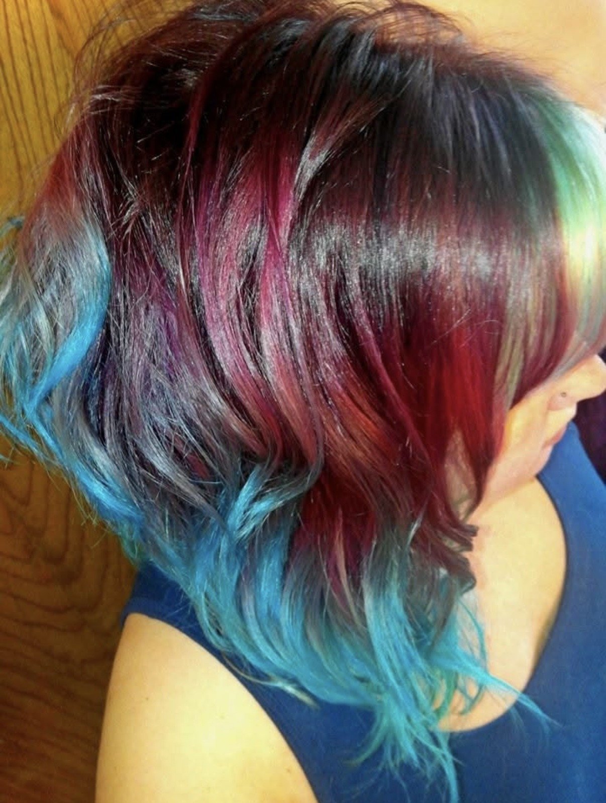 A person with shoulder-length, multicolored hair featuring shades of blue, gray, red, pink, and black, wearing a dark blue top.