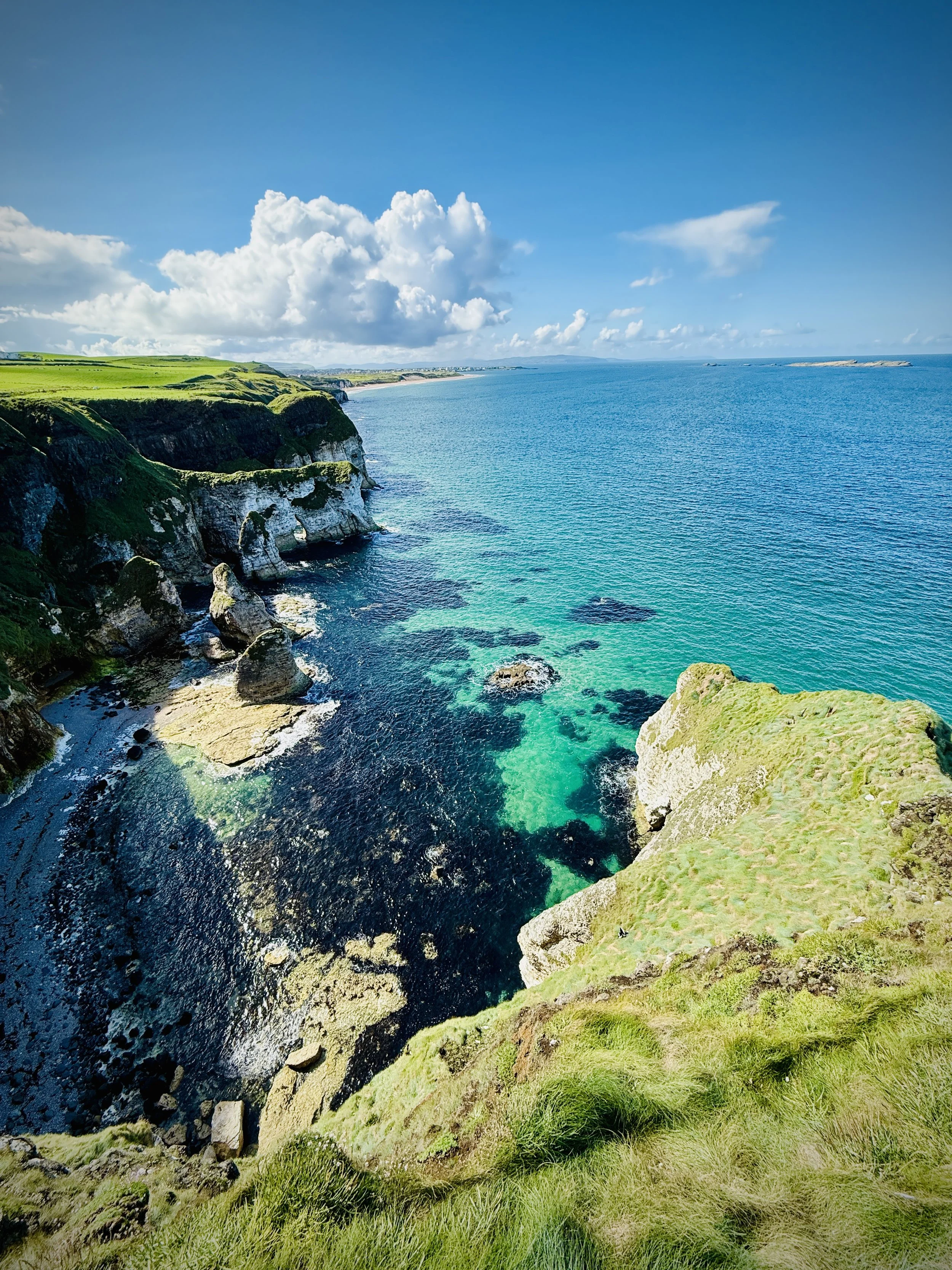 Cliffs with green grass overlooking a blue ocean under a partly cloudy sky.