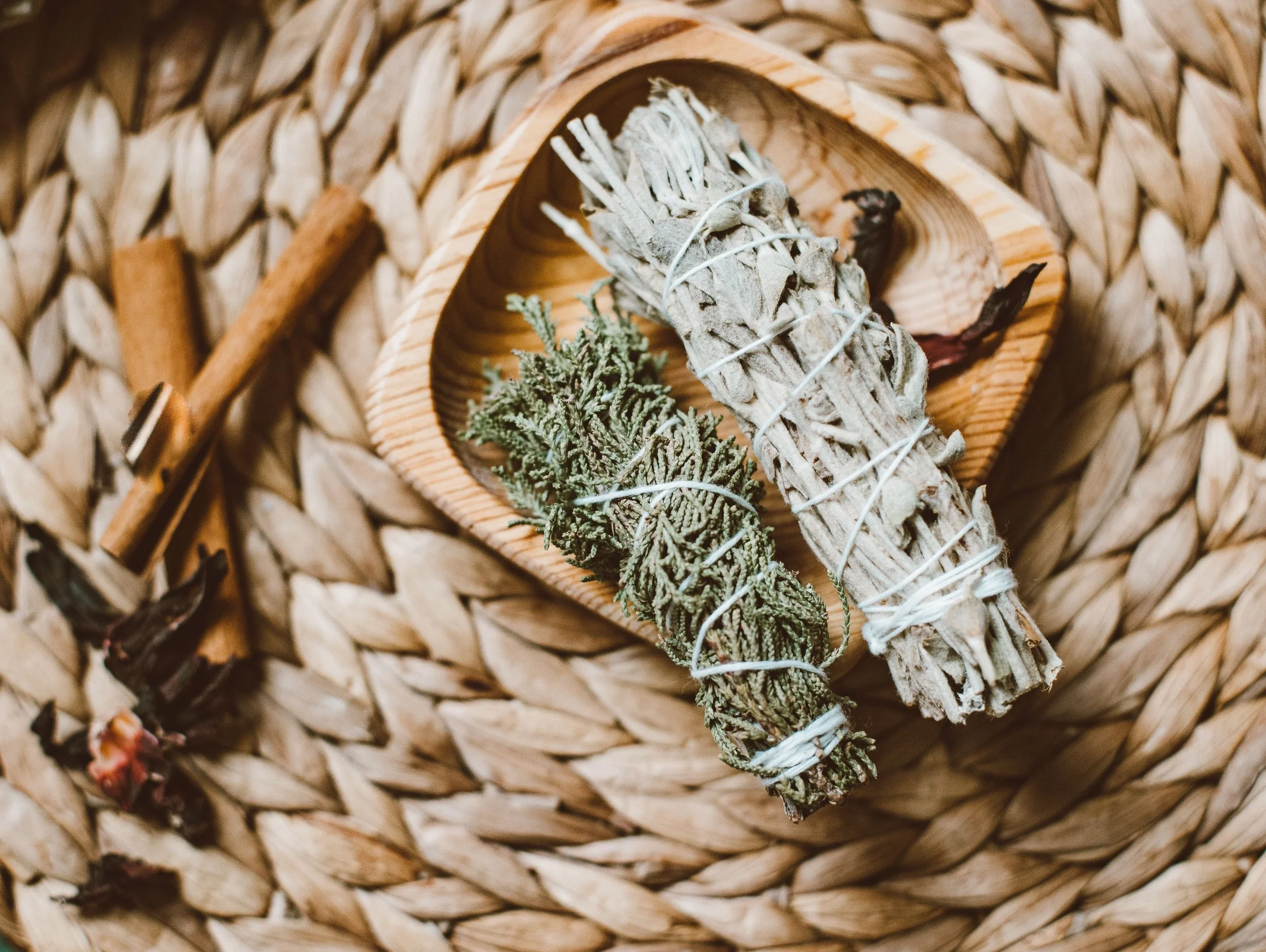 Bundled white sage and dried herbs in a wooden bowl on a woven mat