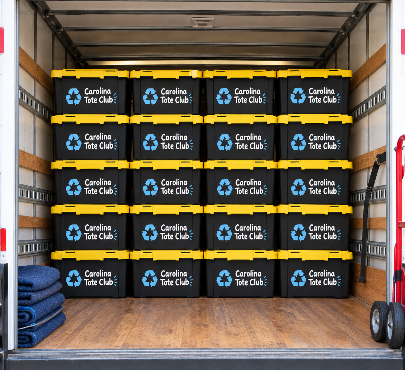 A truck easily filled with black and yellow Carolina Tote Club bins. There are moving blankets on the left and a hand truck on the right inside the truck.
