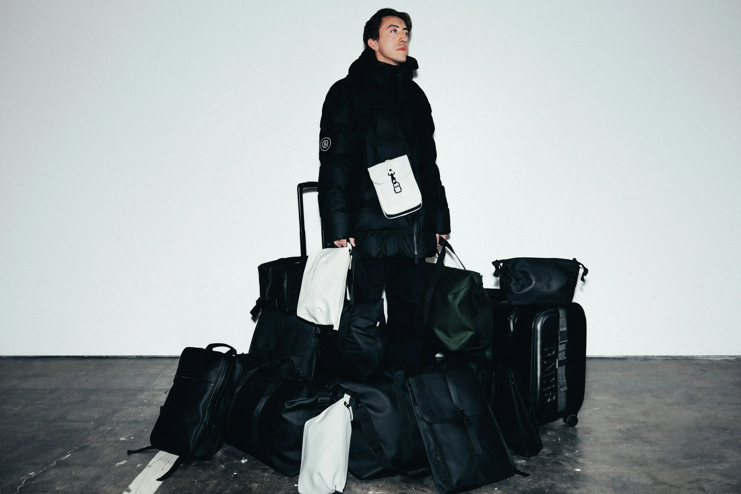 A man standing among various black and white luggage and bags against a plain white wall.