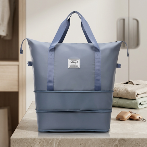 Light blue expandable tote bag with multiple zip compartments, with handles on a countertop, with folded clothes in the background.