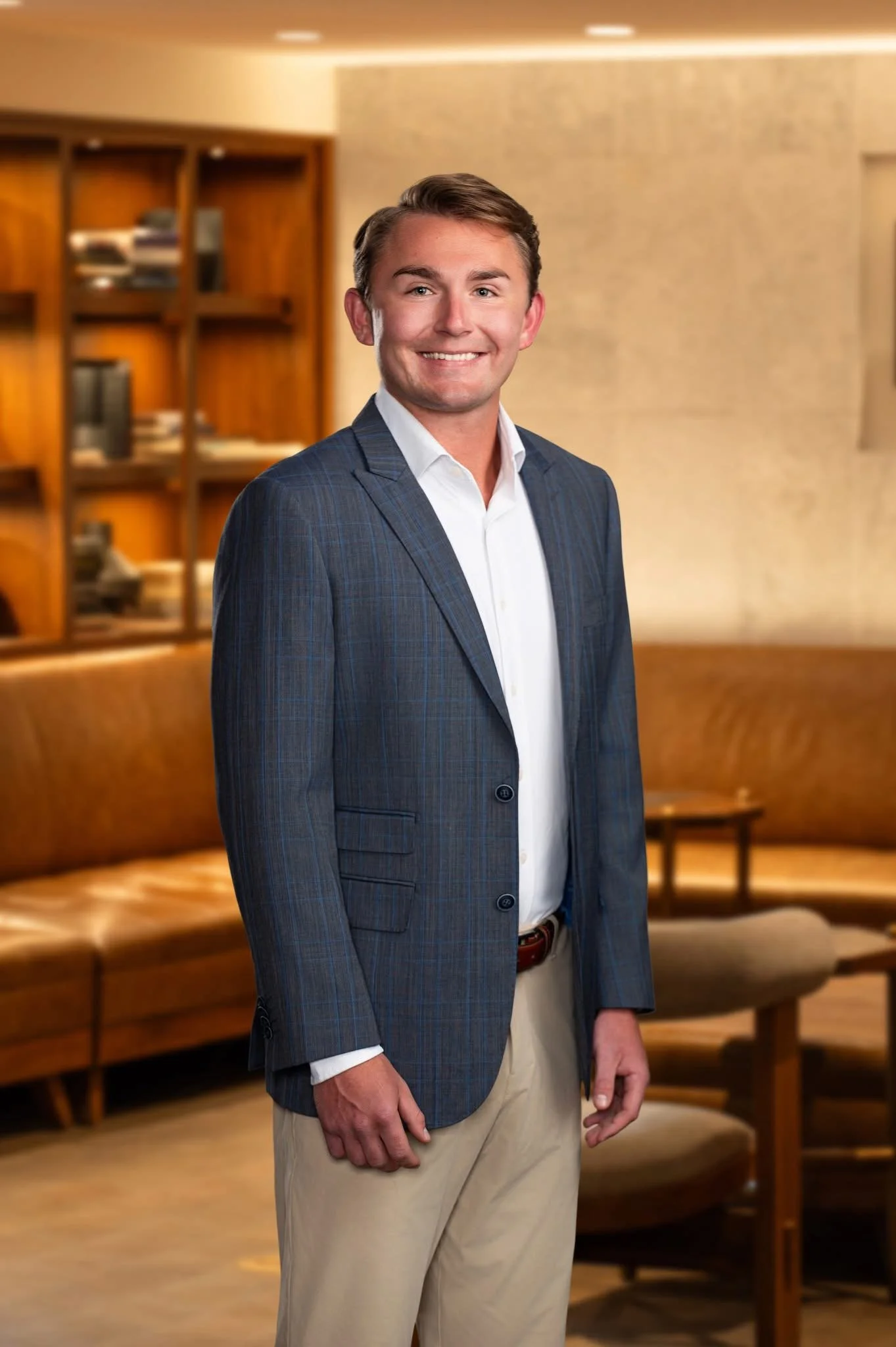 A man in business casual attire smiling in a warmly decorated room with bookshelves and a dining area.