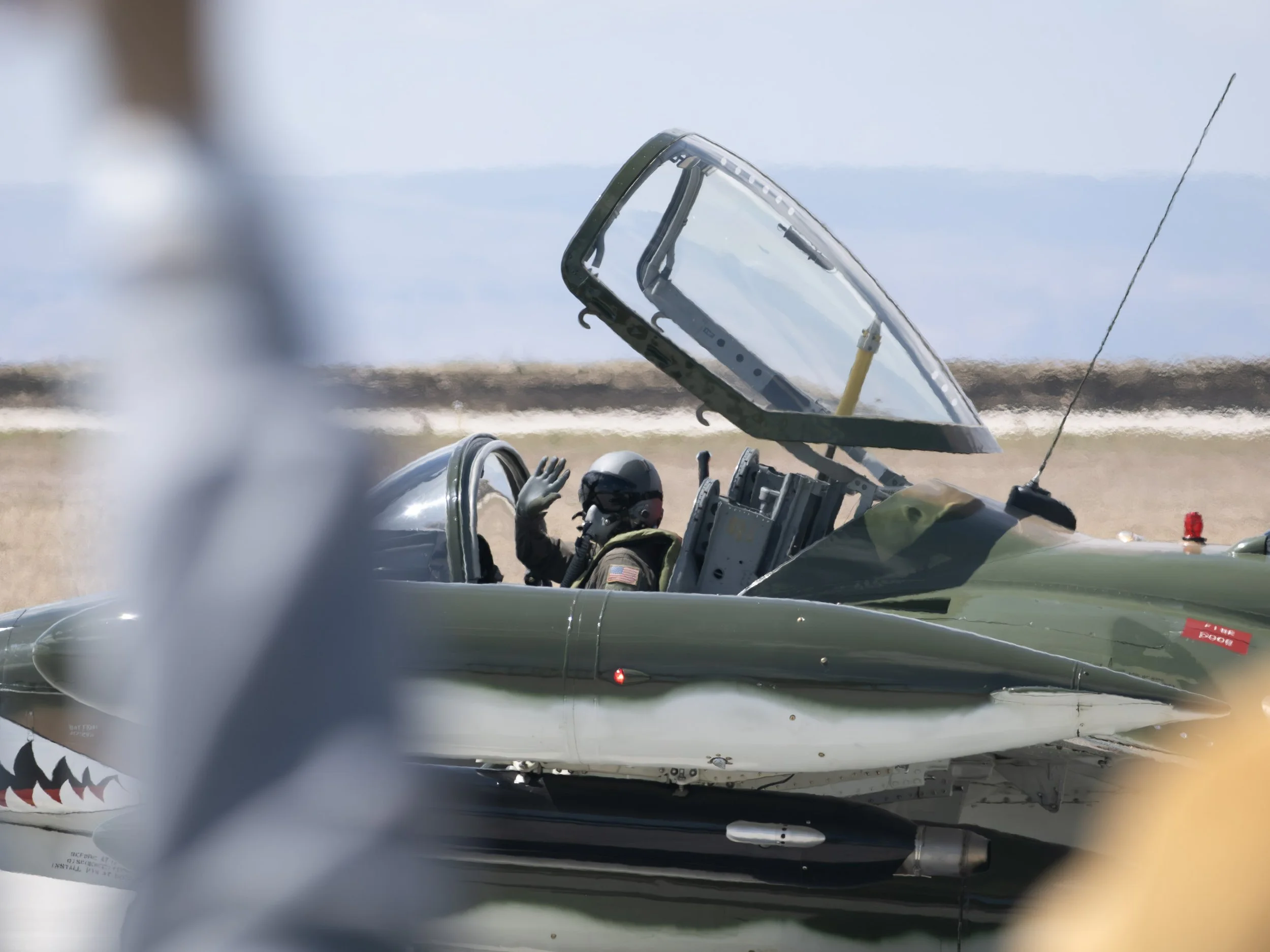 Military fighter jet with an open cockpit, pilot inside, during daytime on a runway.