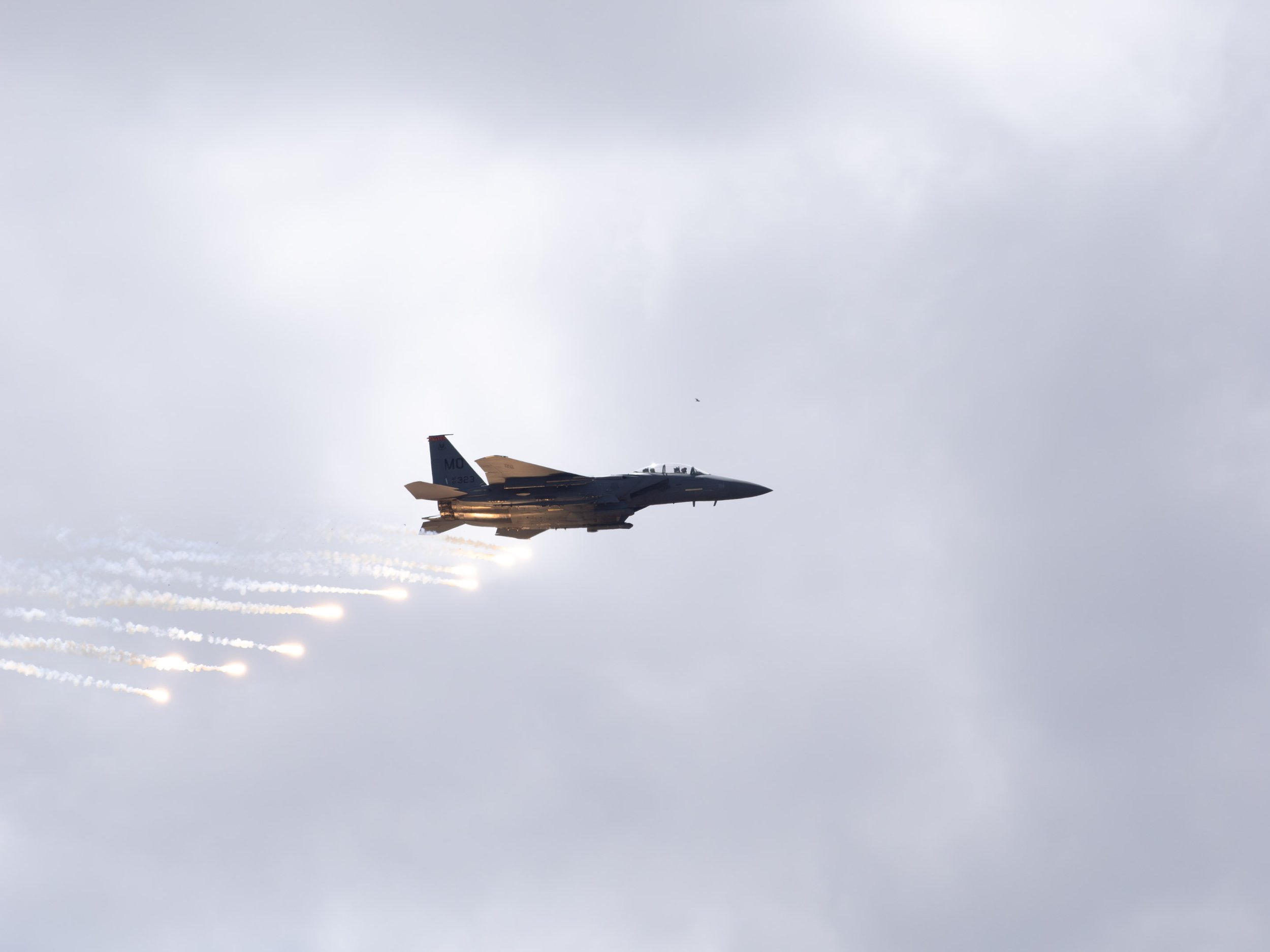 A fighter jet flying high in the cloudy sky with vapor trails behind it.