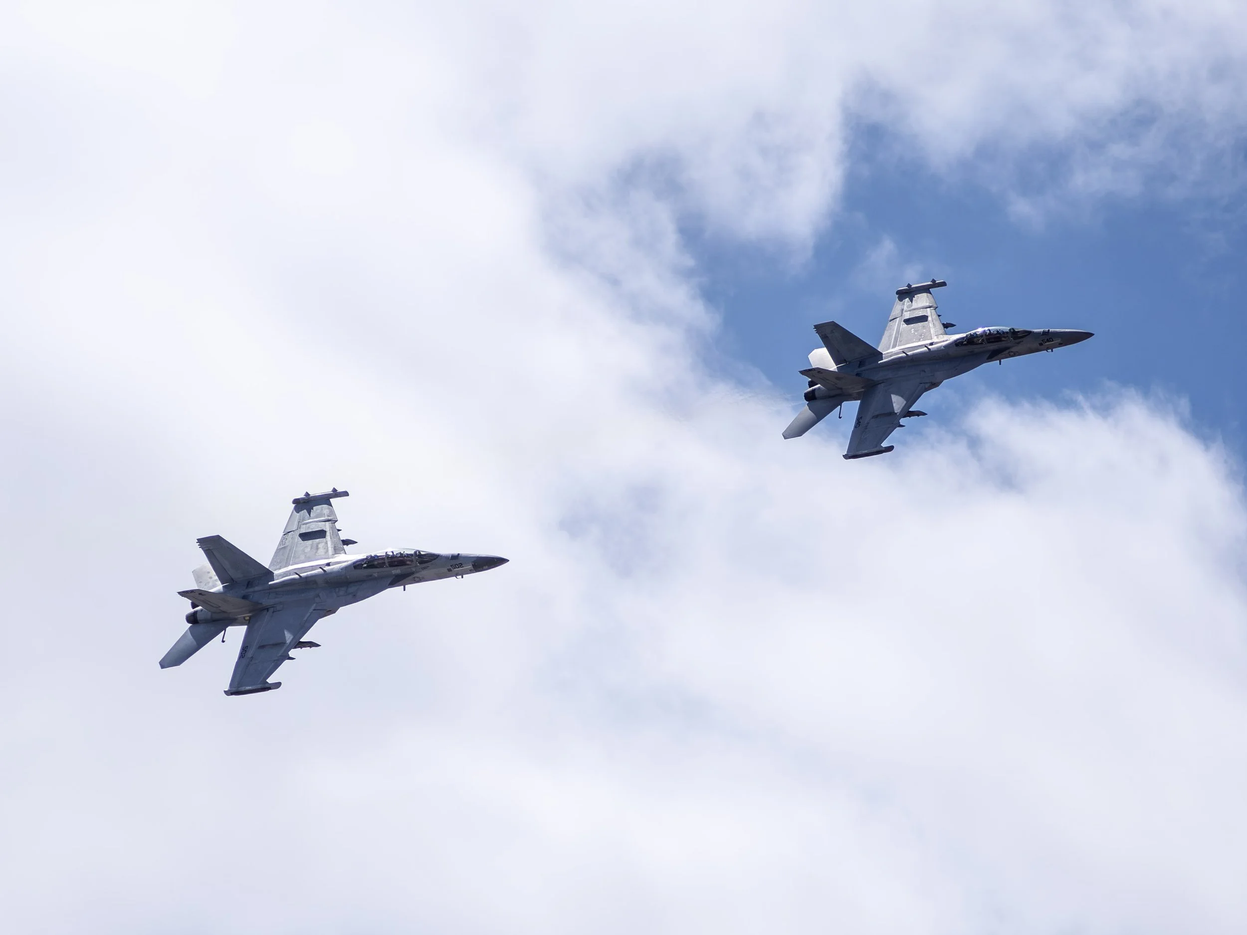 Two fighter jets flying in formation through a cloudy sky.