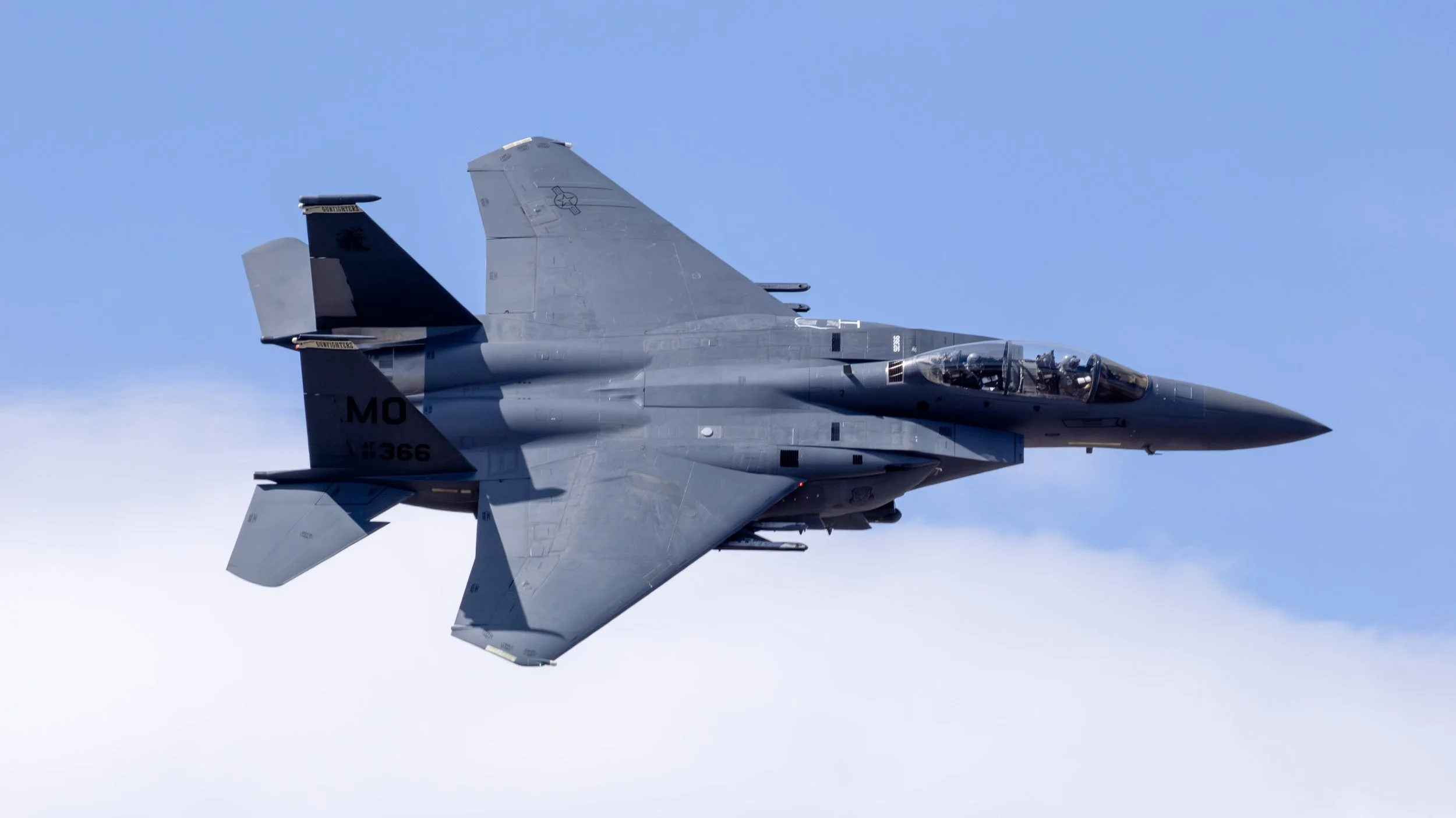 Fighter jet flying in the sky with blue clouds.