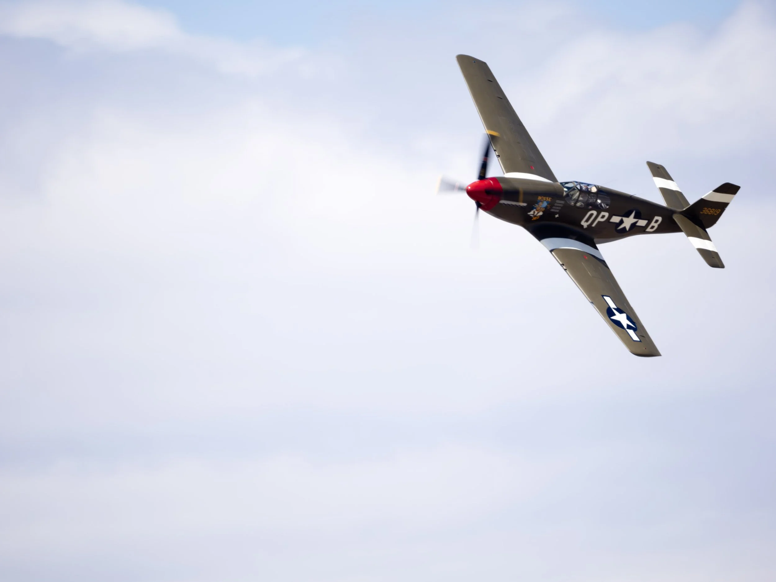 A vintage military aircraft flying in the sky with a blue clouded backdrop.