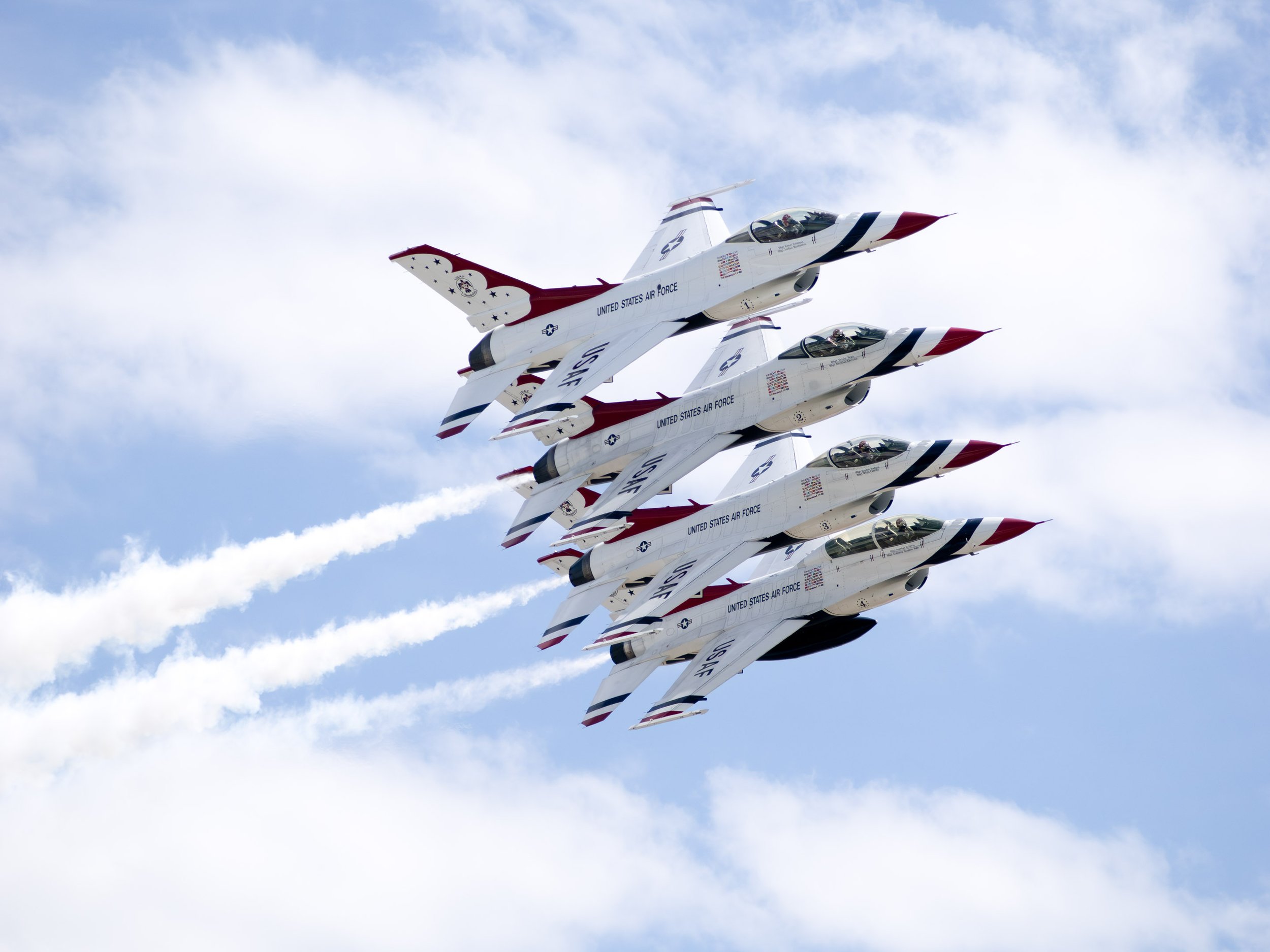 Four United States Air Force fighter jets flying in a tight formation against a partly cloudy sky.