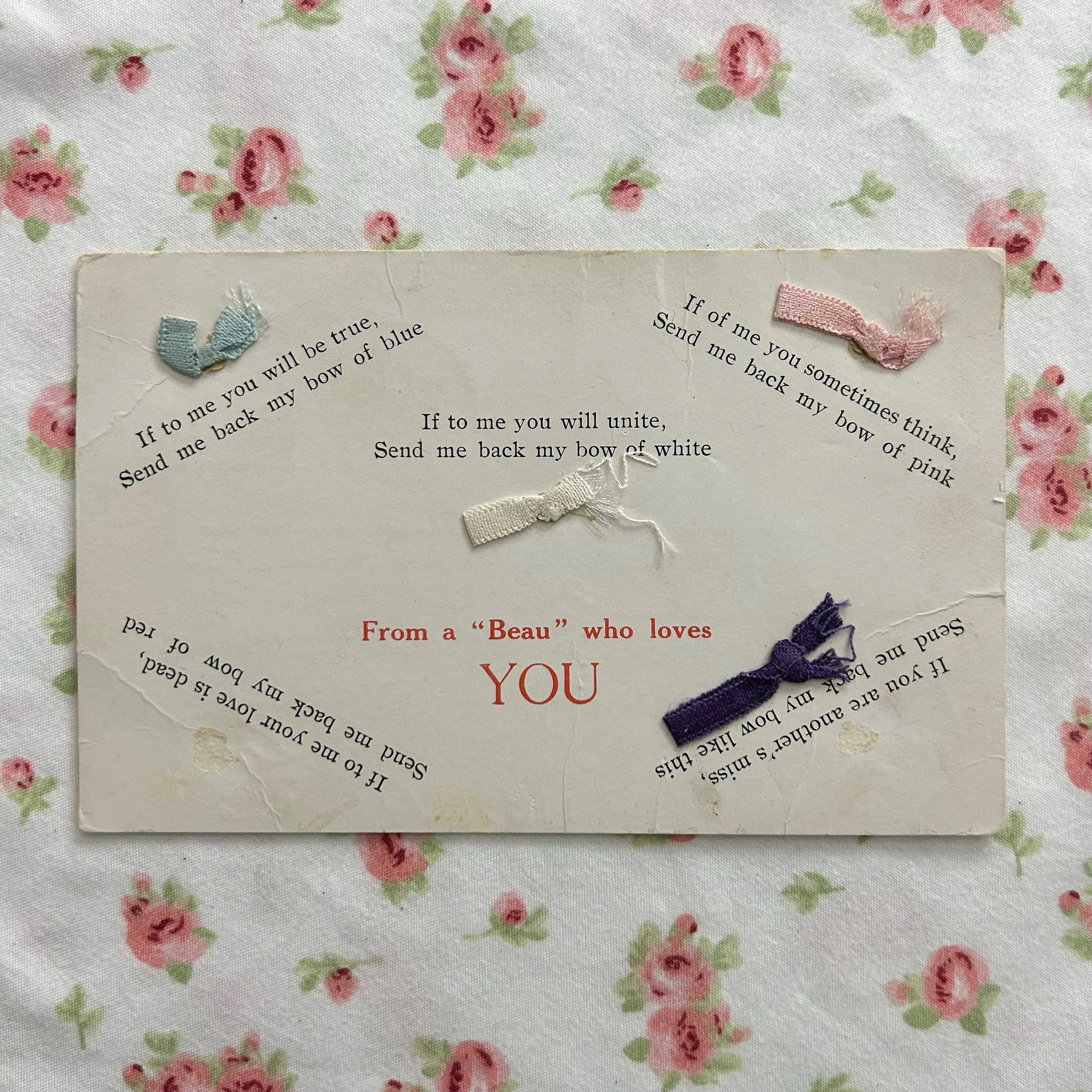Close-up of a torn piece of paper with text, decorated with small pastel-colored ribbons, placed on a floral patterned fabric background.
